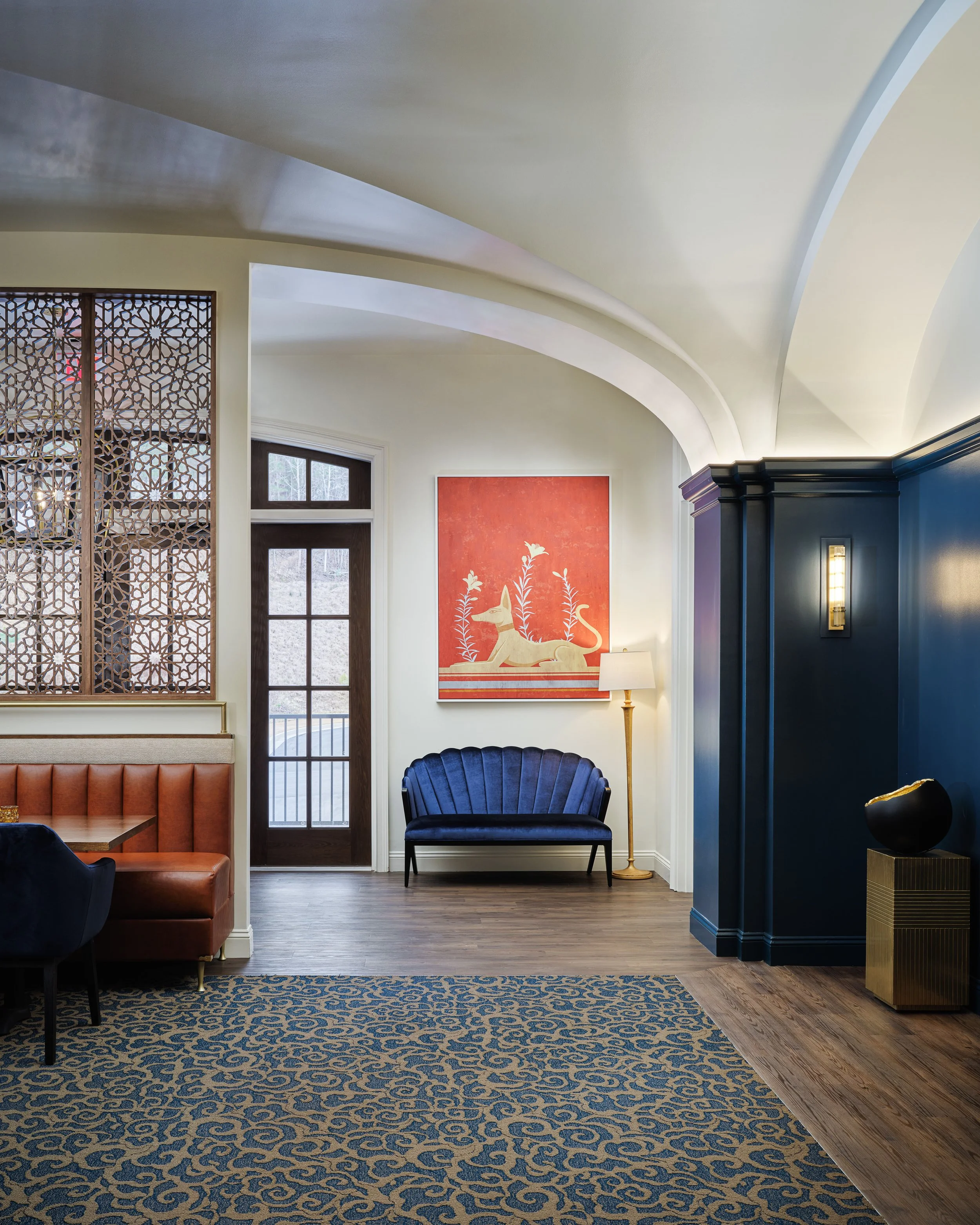Off The Rails entry with a navy velvet settee, curved ceiling, carved screen, and red equestrian artwork, designed by Ashley Schneider