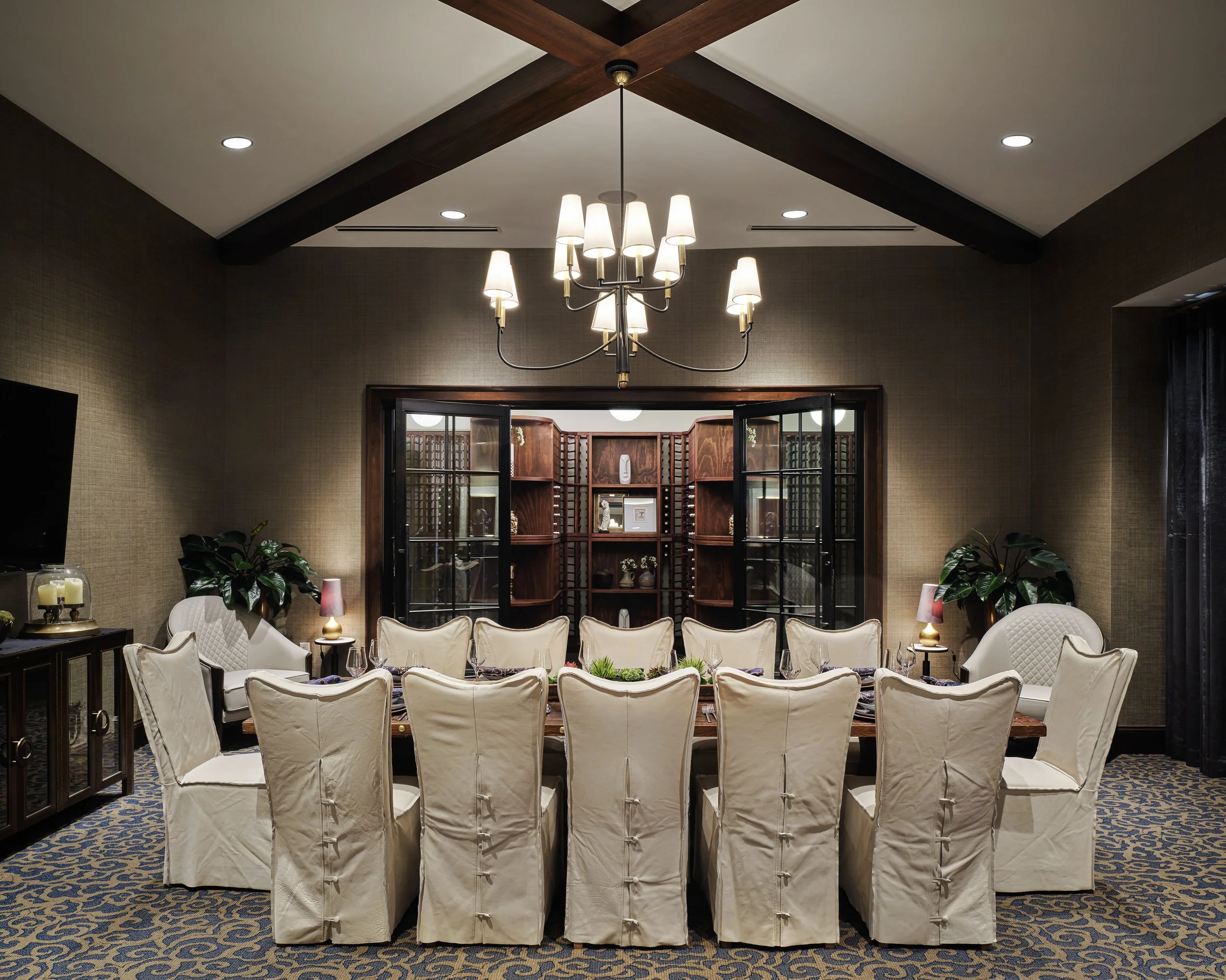 Private dining room with slipcovered chairs, cathedral ceiling with wood beams, brass chandelier, and glass-front wine cellar, Off The Rails restaurant and bar, Woodstock, GA, interior design by Ashley Schneider