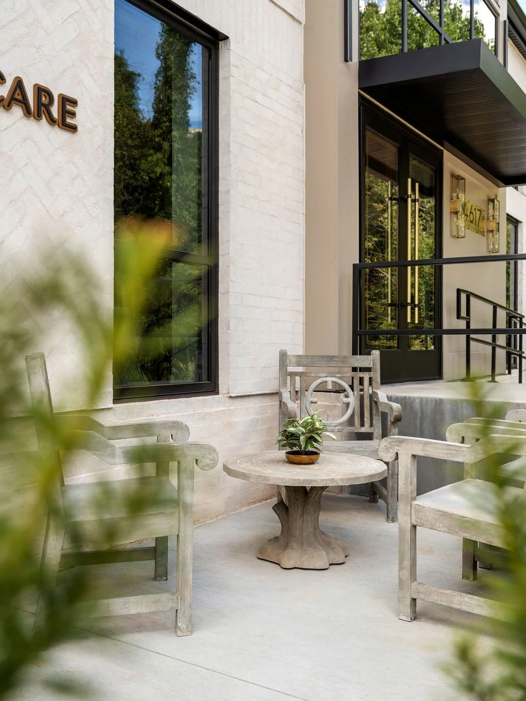 Boutique commercial outdoor seating area with weathered stone armchairs and pedestal table beside white brick exterior, interior design by Luxe Style Studio