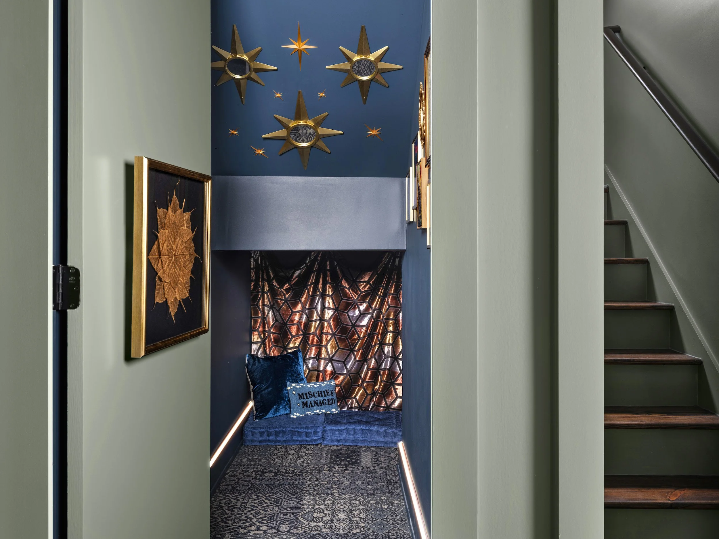 Dramatic under-stair hidden secret nook with navy blue walls, gold starburst wall sculptures, metallic geometric fabric, LED floor lighting, and blue velvet cushions, Atlanta, GA private residence, interior design by Luxe Style Studio