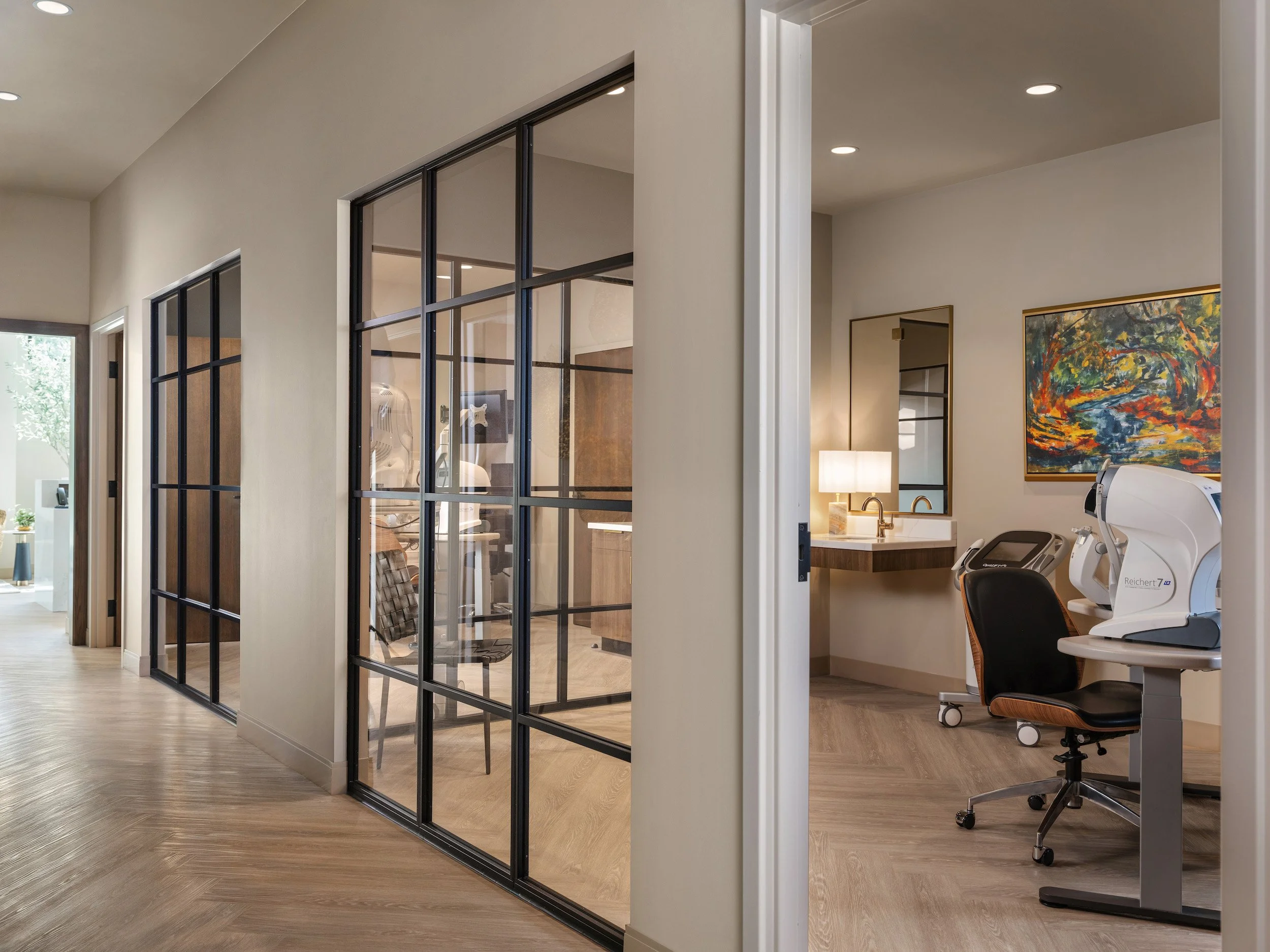 Luxury optometry office corridor with black steel and glass partitions revealing exam rooms, herringbone wood floors, and natural light, Windsor Eye Care optical boutique, Atlanta, GA, interior design by Luxe Style Studio