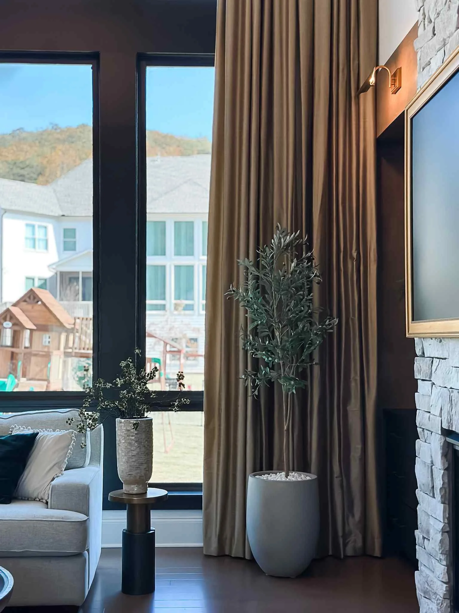 Dramatic floor-to-ceiling caramel velvet drapes beside tall black-frame windows and stone fireplace, Luxe Style Studio