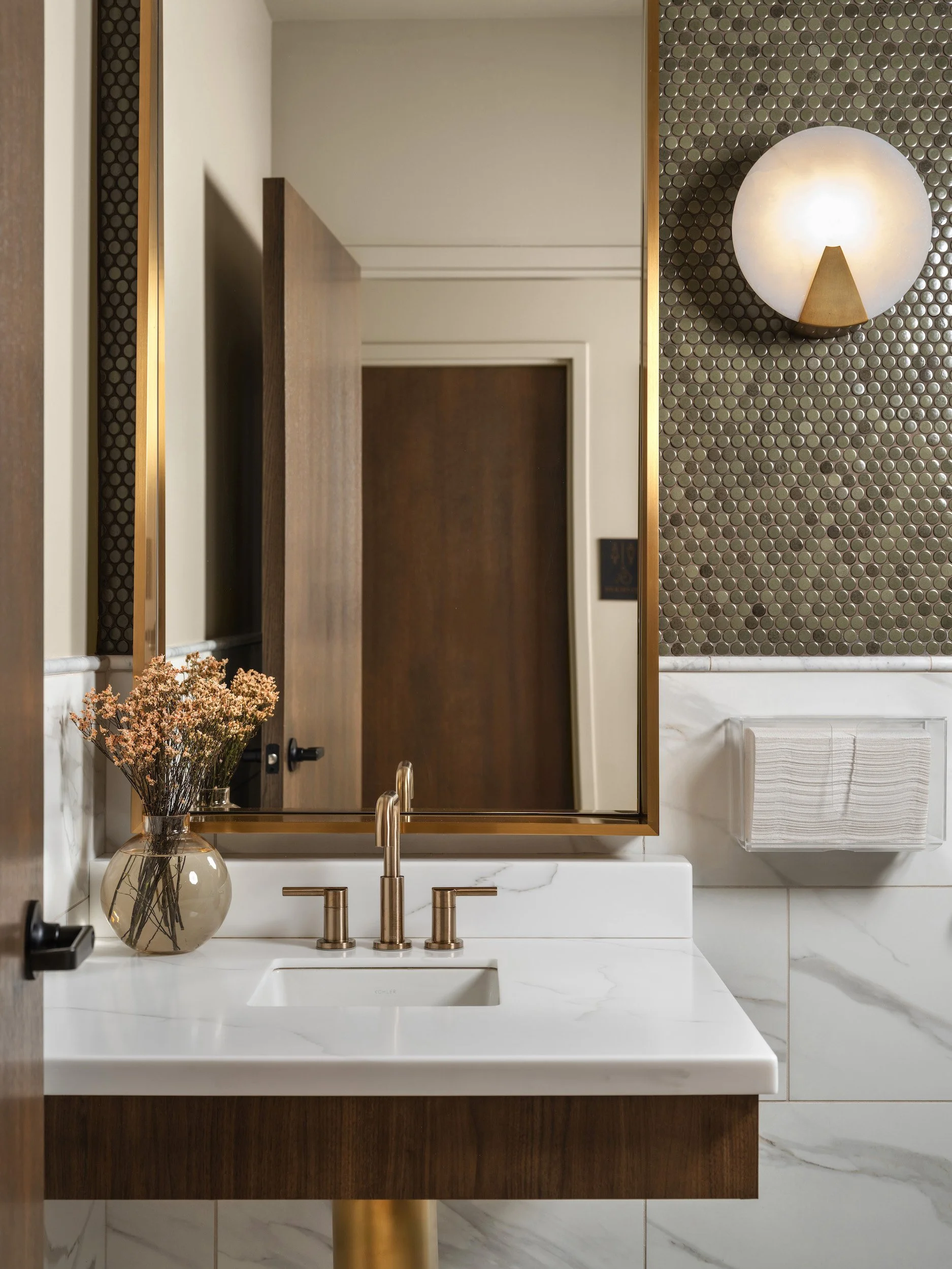 Powder room with metallic penny tile, a brass-framed mirror, globe sconce, and marble vanity, designed by Luxe Style Studio