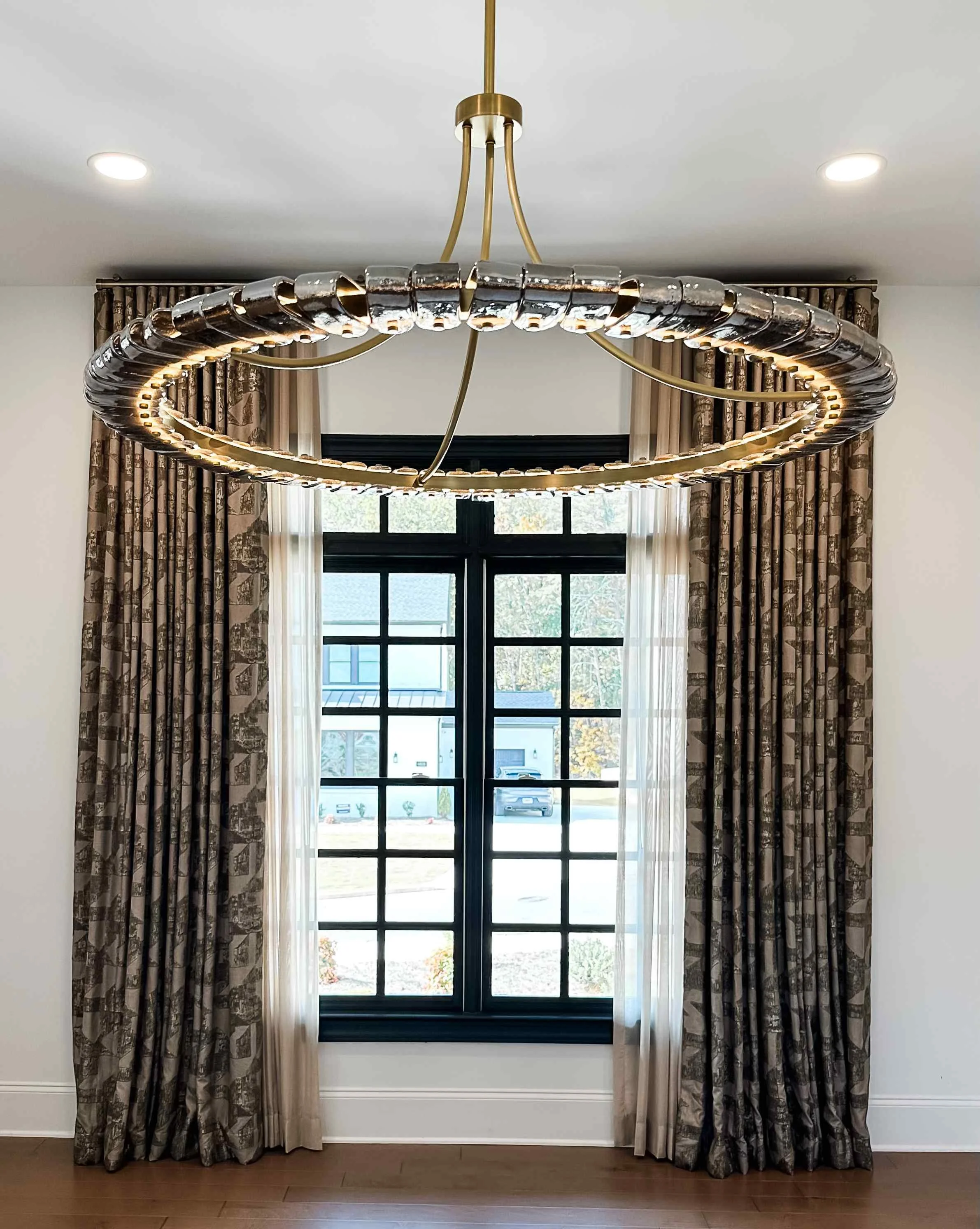 Large circular crystal and brass halo chandelier above toile-printed drapery panels in dining room by Luxe Style Studio