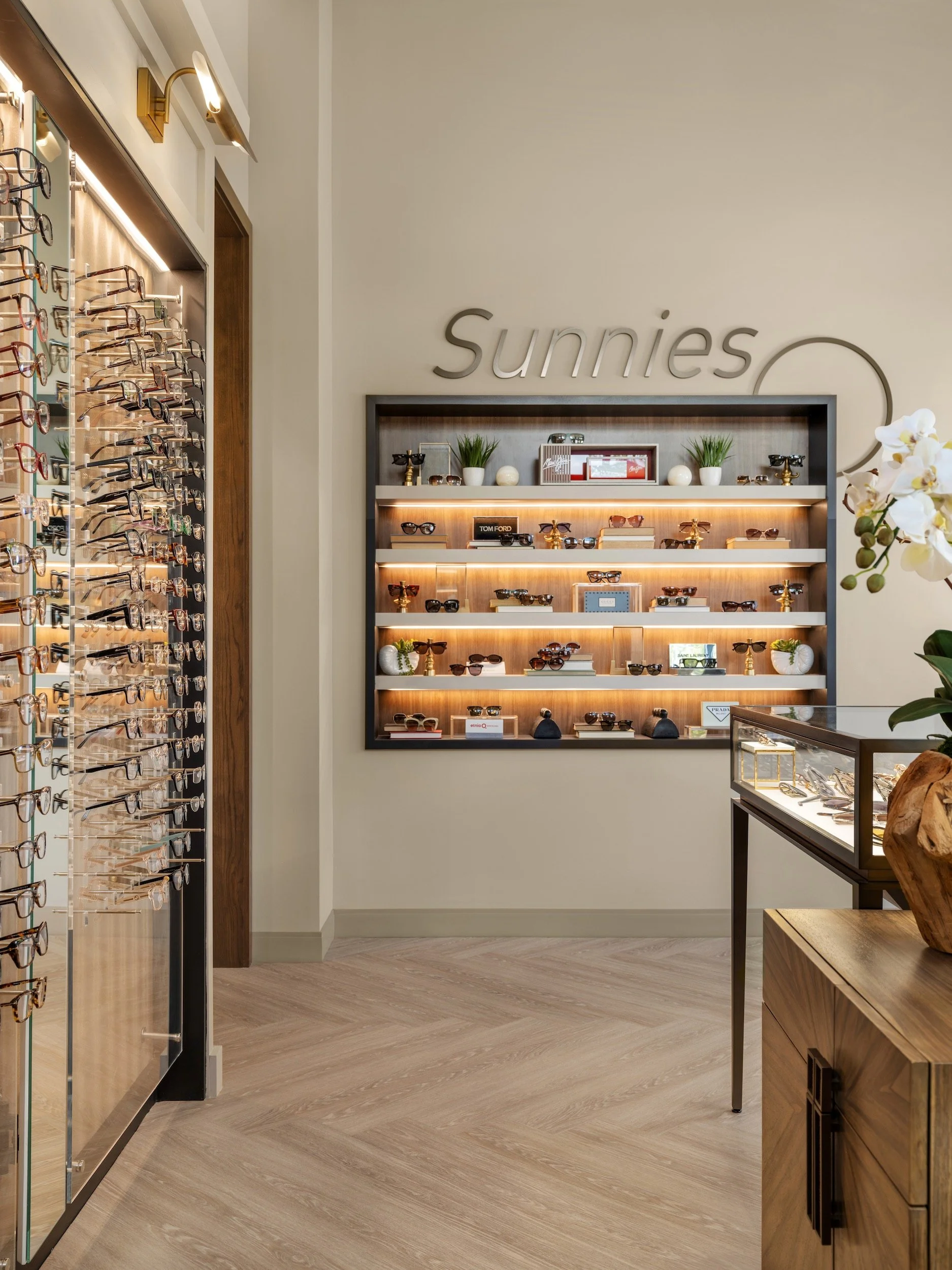 Boutique sunglasses display wall with backlit wood shelving, designer eyewear, and decorative styling in luxury optical office interior, Windsor Eye Care optical boutique, Atlanta, GA, interior design by Luxe Style Studio