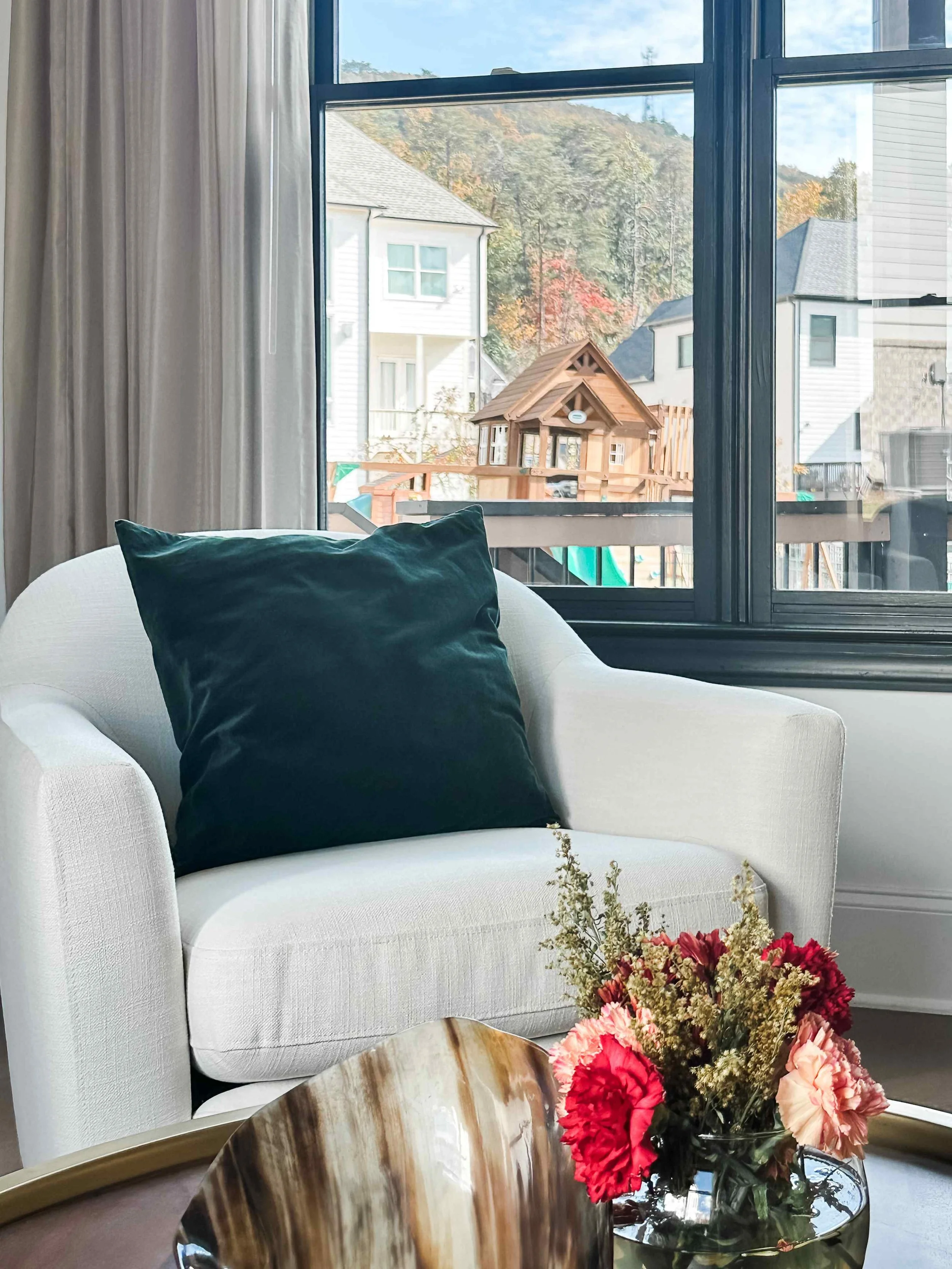 White curved accent chair with emerald velvet pillow beside black-frame window, styled by Luxe Style Studio