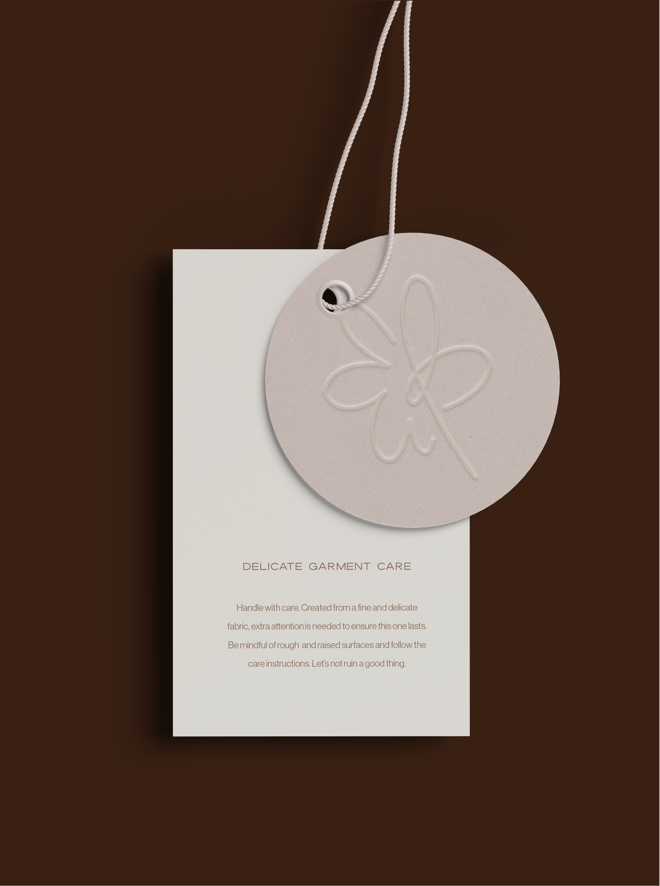 A white tag with text labeled 'Delicate Garment Care' hanging from a grey, round tag with embossed flower design. The background is brown.