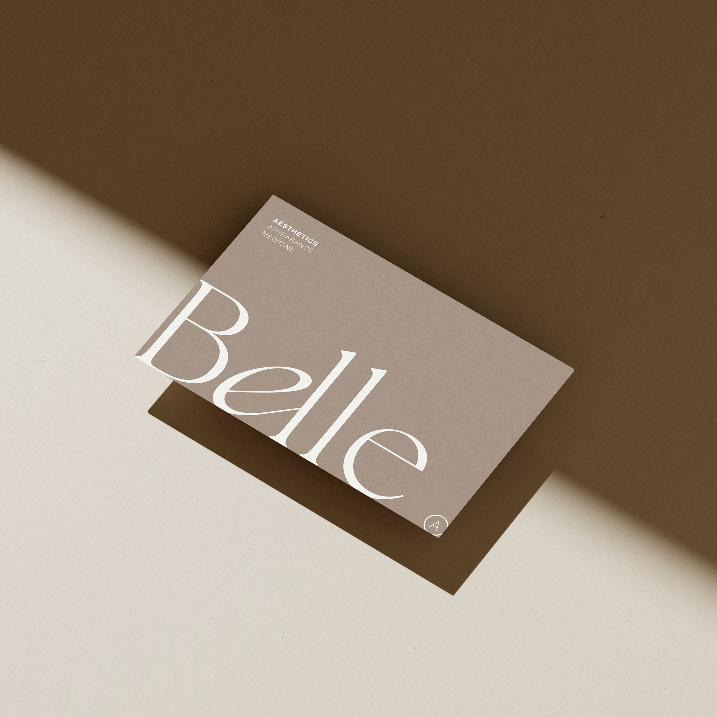 A beige card with the words "Belle" in large white letters, placed on a surface with light and shadow creating a minimalist aesthetic.
