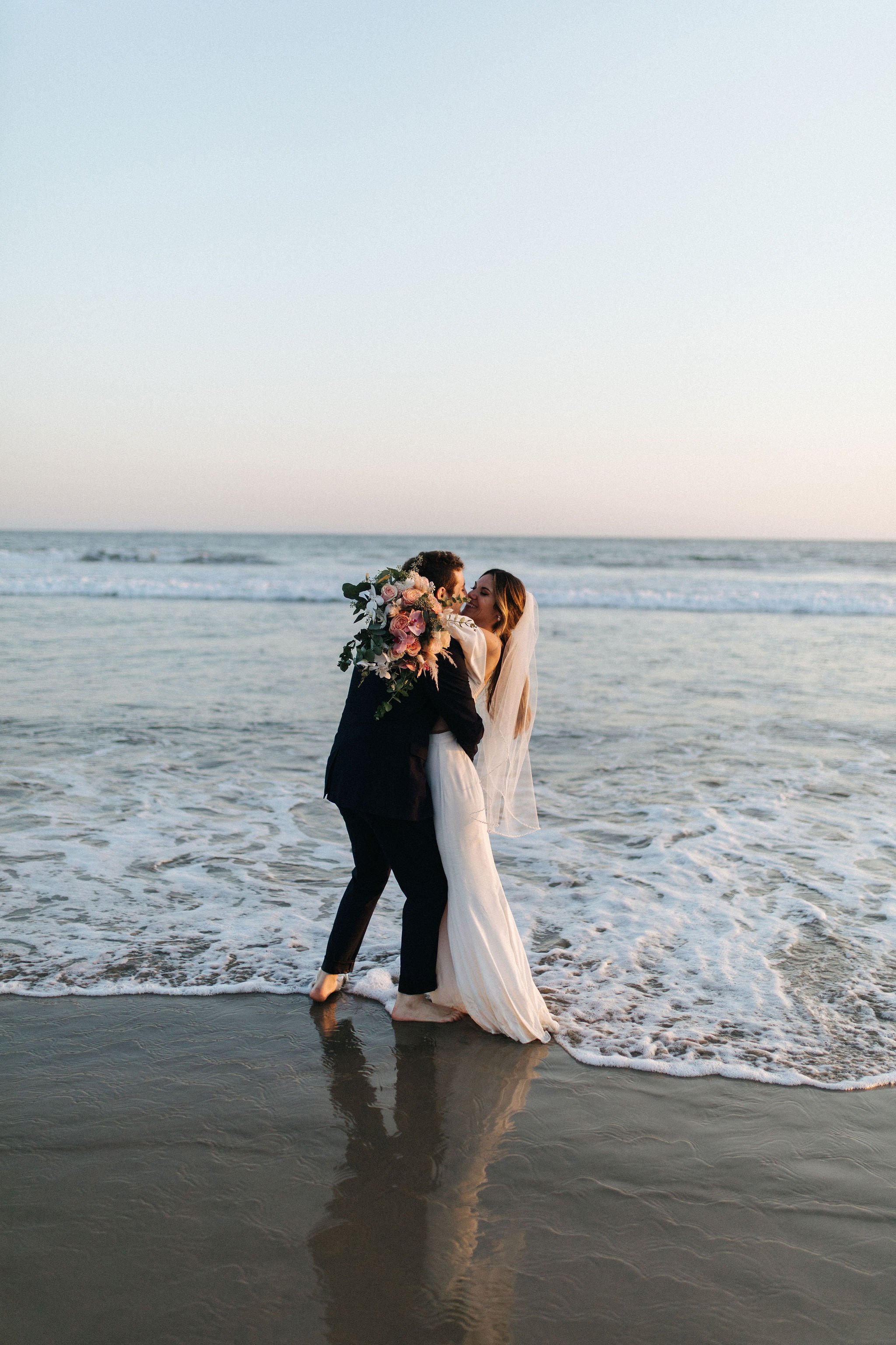 bride and groom walk along the beach after just getting married in malibu