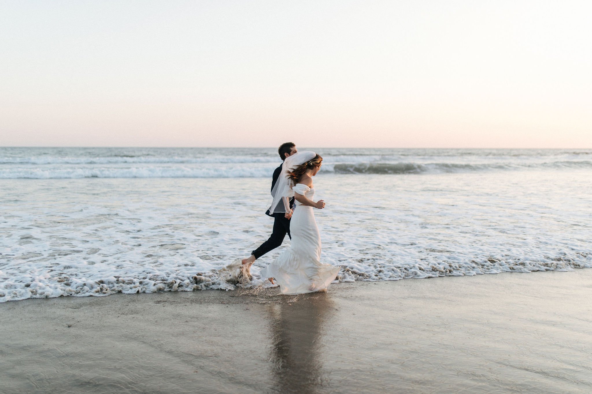 couple runs along the beach at sunset in malibu after their destination wedding at malibu west beach club