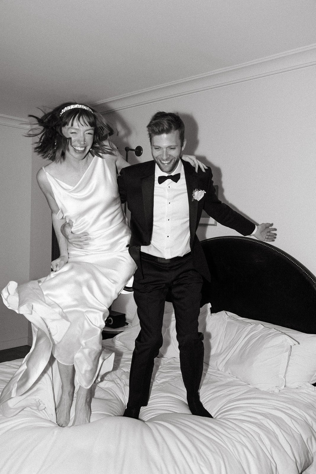 flash photography of bride and groom jumping on the bed after eloping