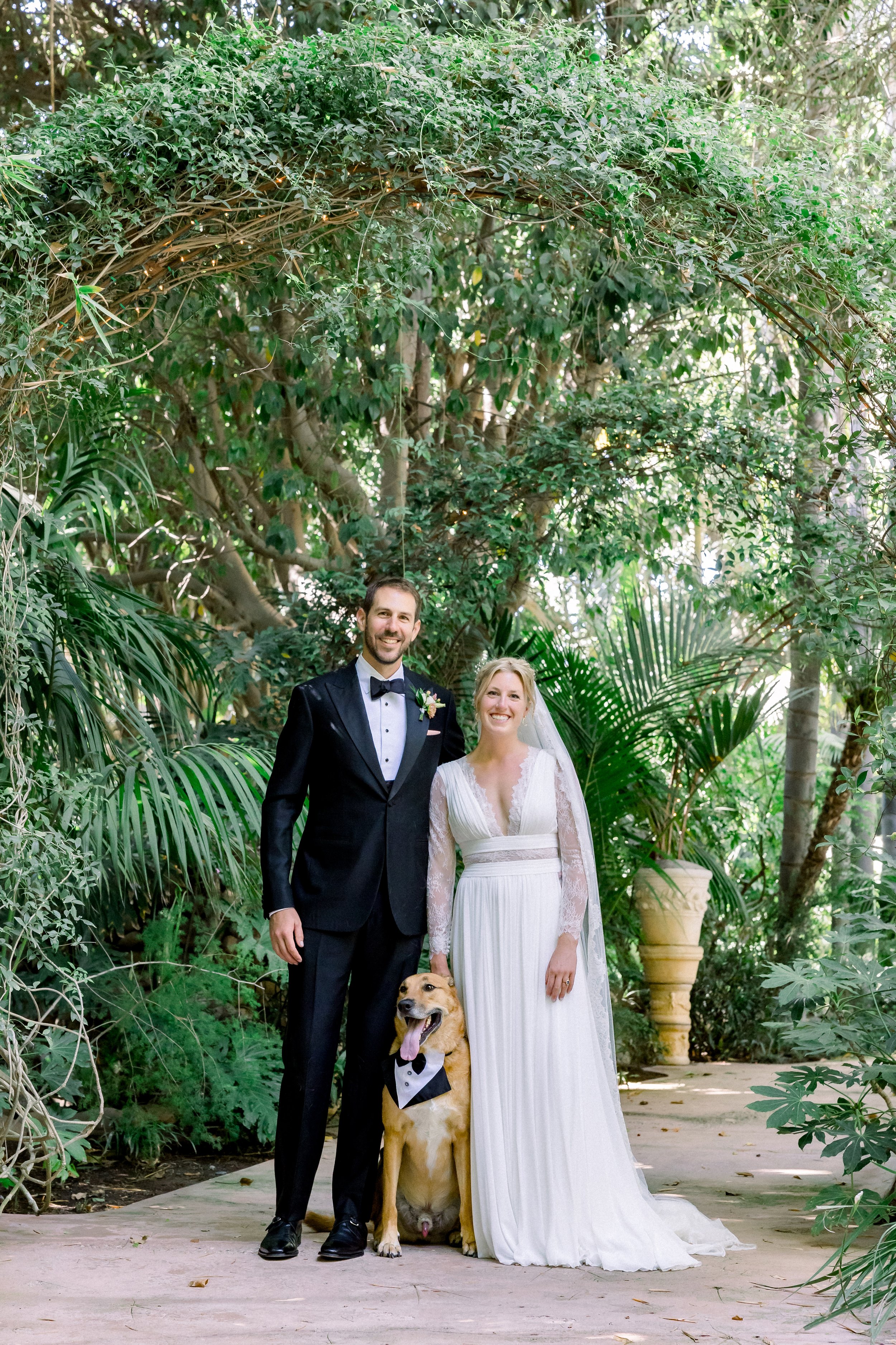 bride and groom pose for wedding day photos with their dog