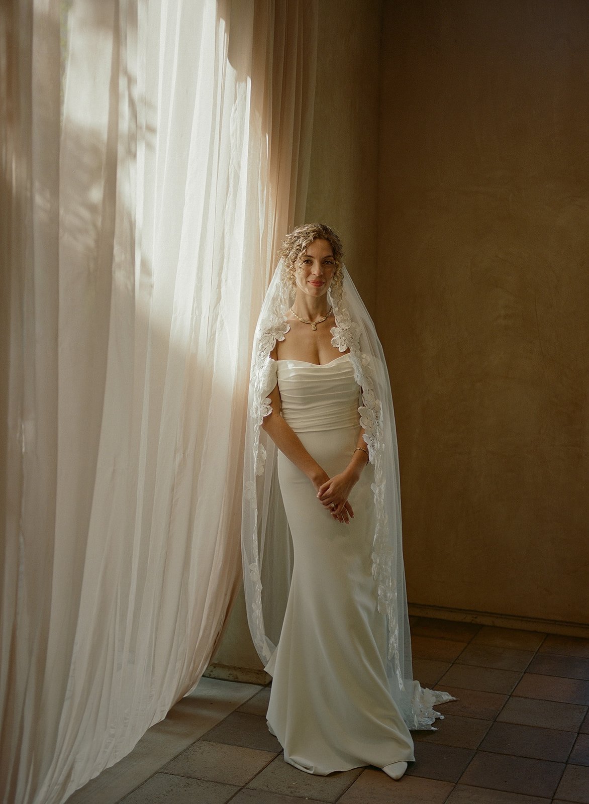 bride with naturally curly hair into an updo hairstyle. Bride's makeup is natural, airbrushed, and not overdone.