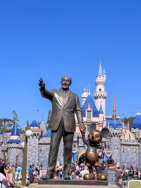 statue of walt disney and mickey mouse in front of disneyland castle