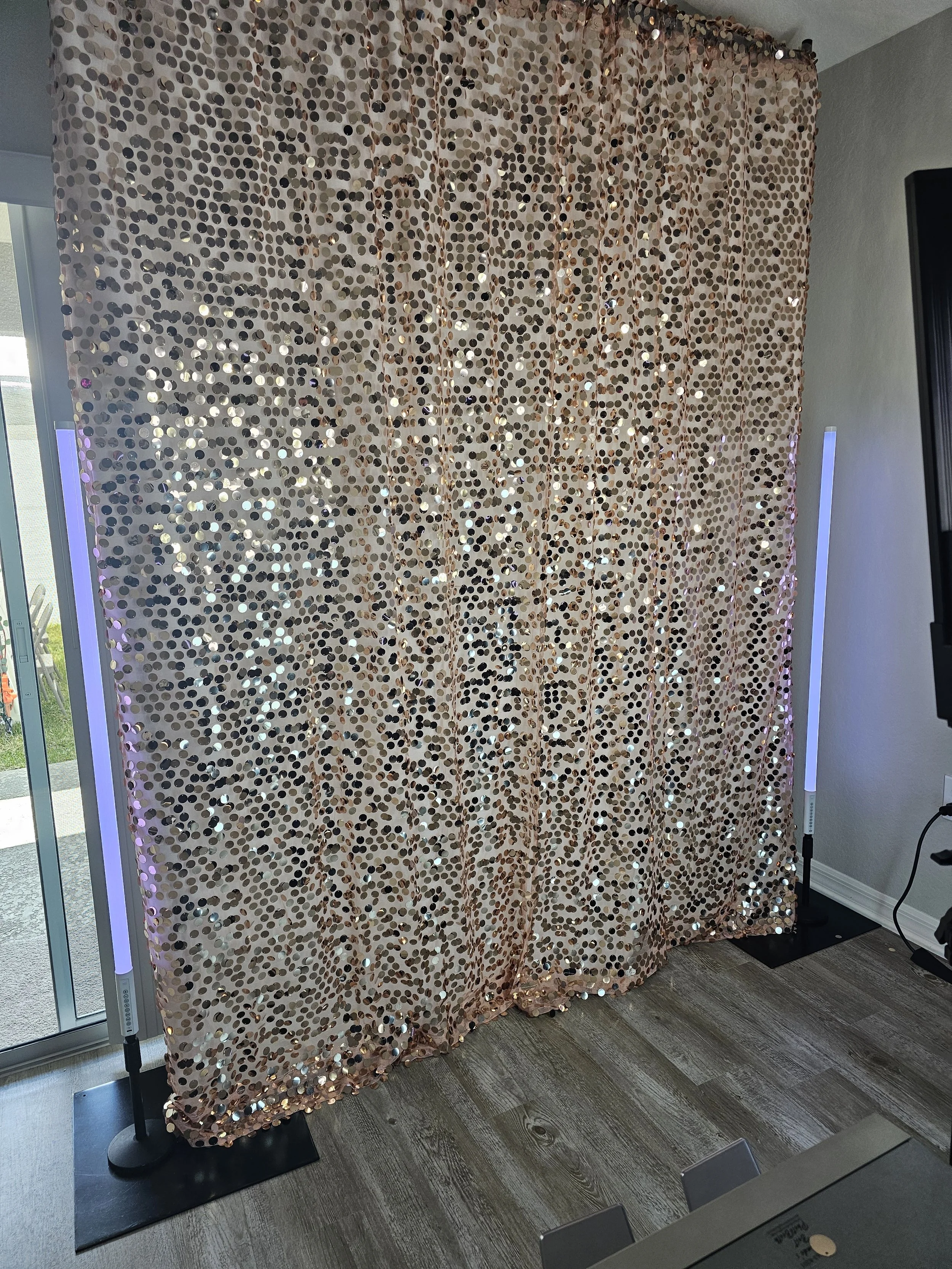 Gold sequin curtain with purple LED lights on either side, set inside a room near a sliding glass door.