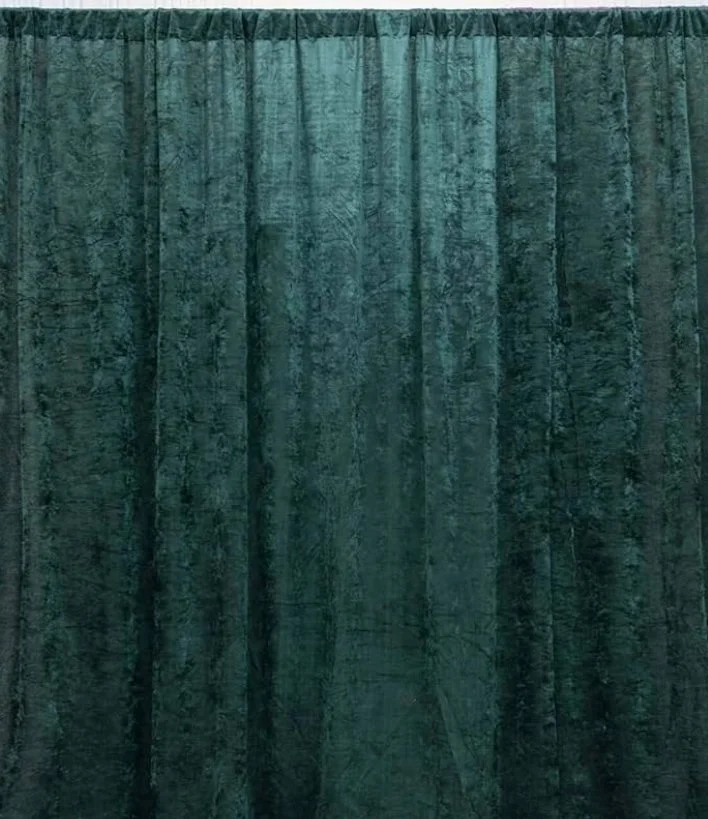 Green velvet curtain with pleats hanging from a rod.