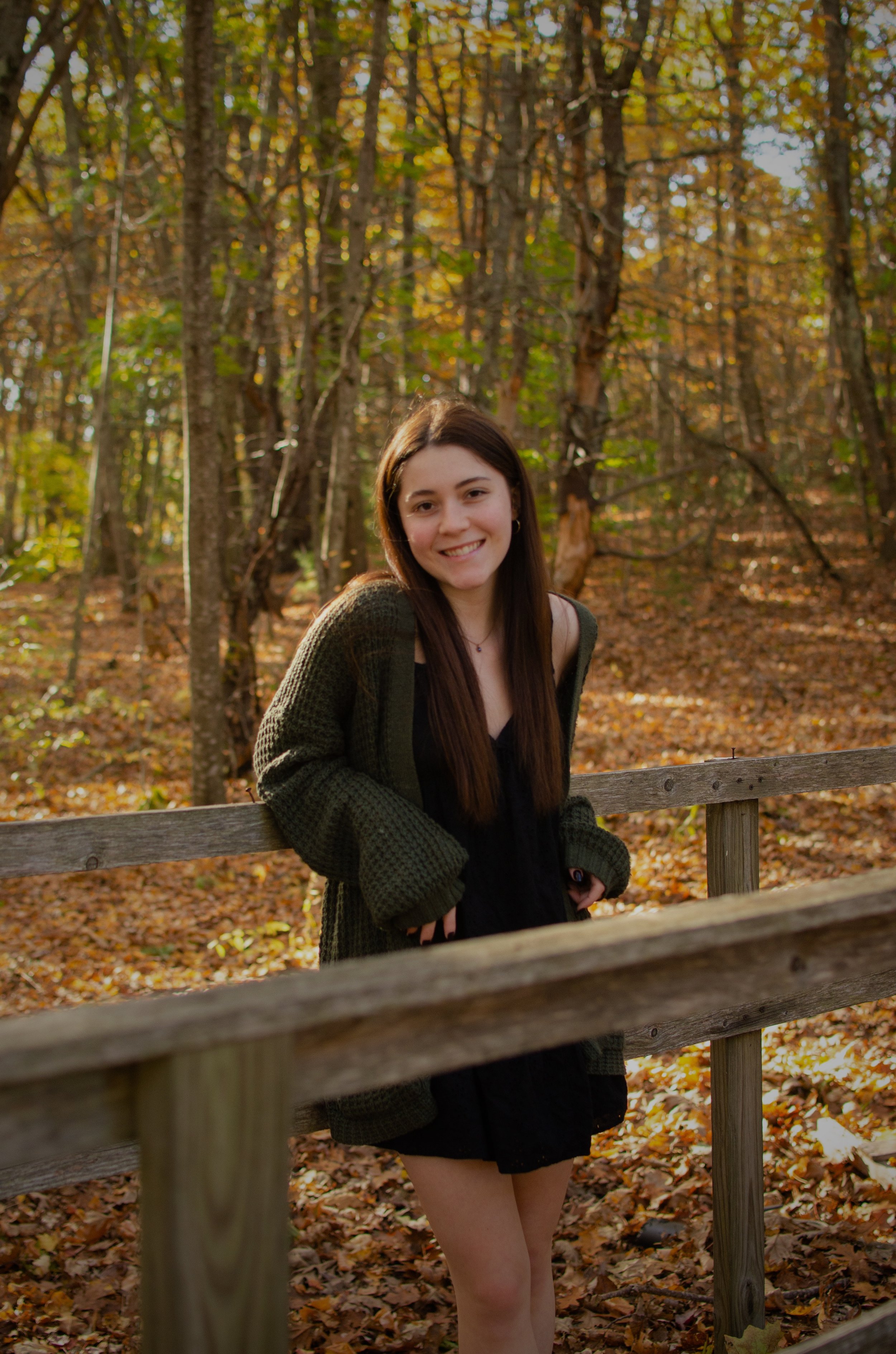 Sophia, desk lead concierge, smiles while sitting outdoors at a wooden railing surrounded by trees.