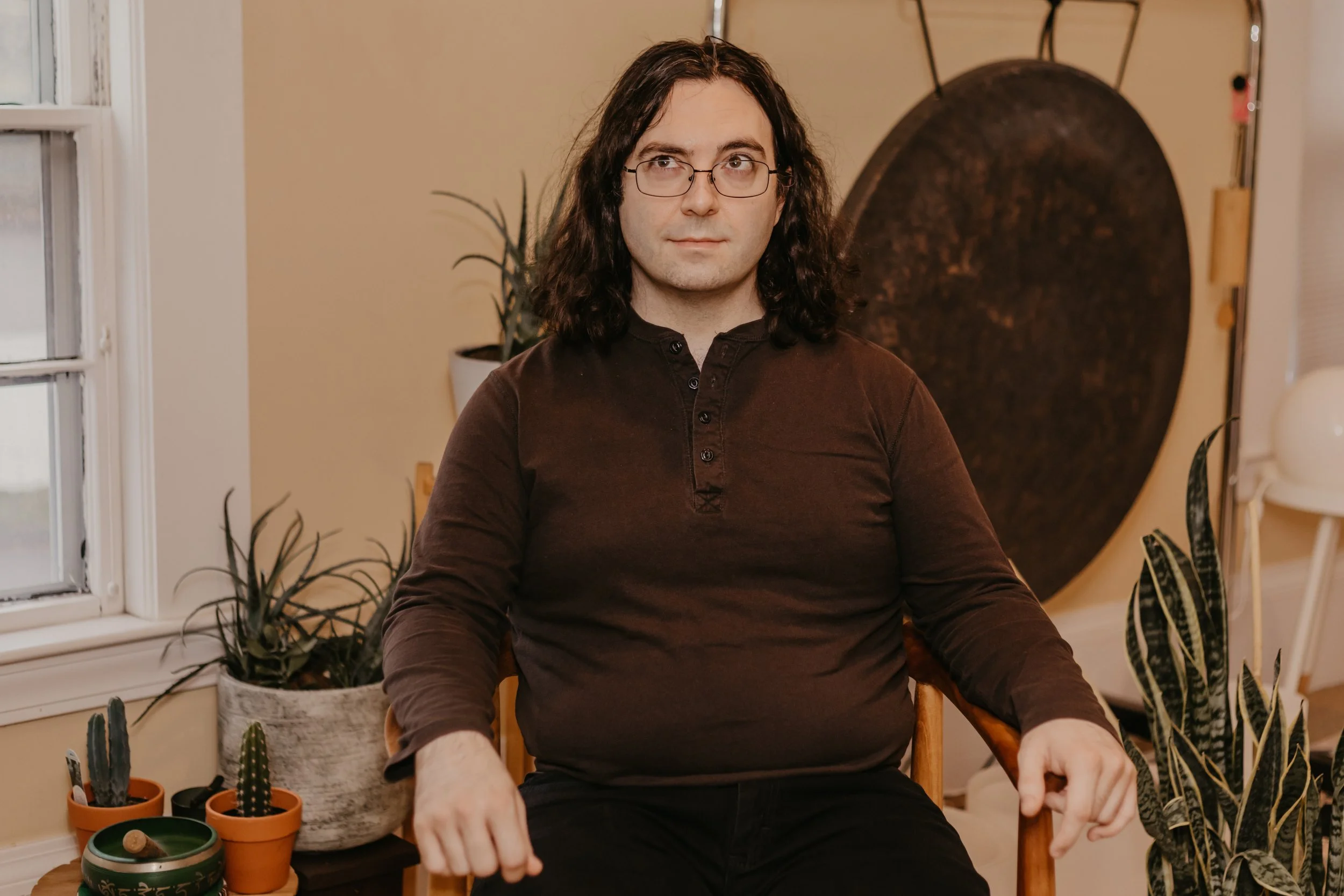 Doug M., master massage therapist specializing in orthopedic massage, smiles while seated indoors wearing a blue button-up shirt.