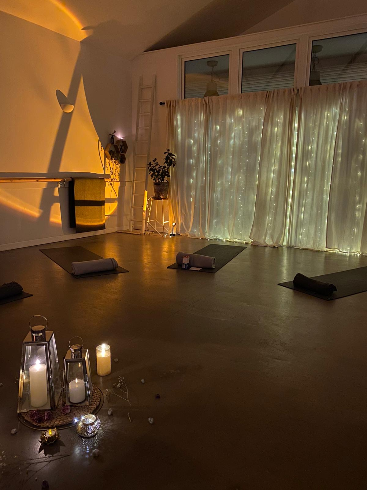 A dimly lit yoga studio decorated with candles and fairy lights, with yoga mats and rolled towels on the floor for a holistic event in bristol.