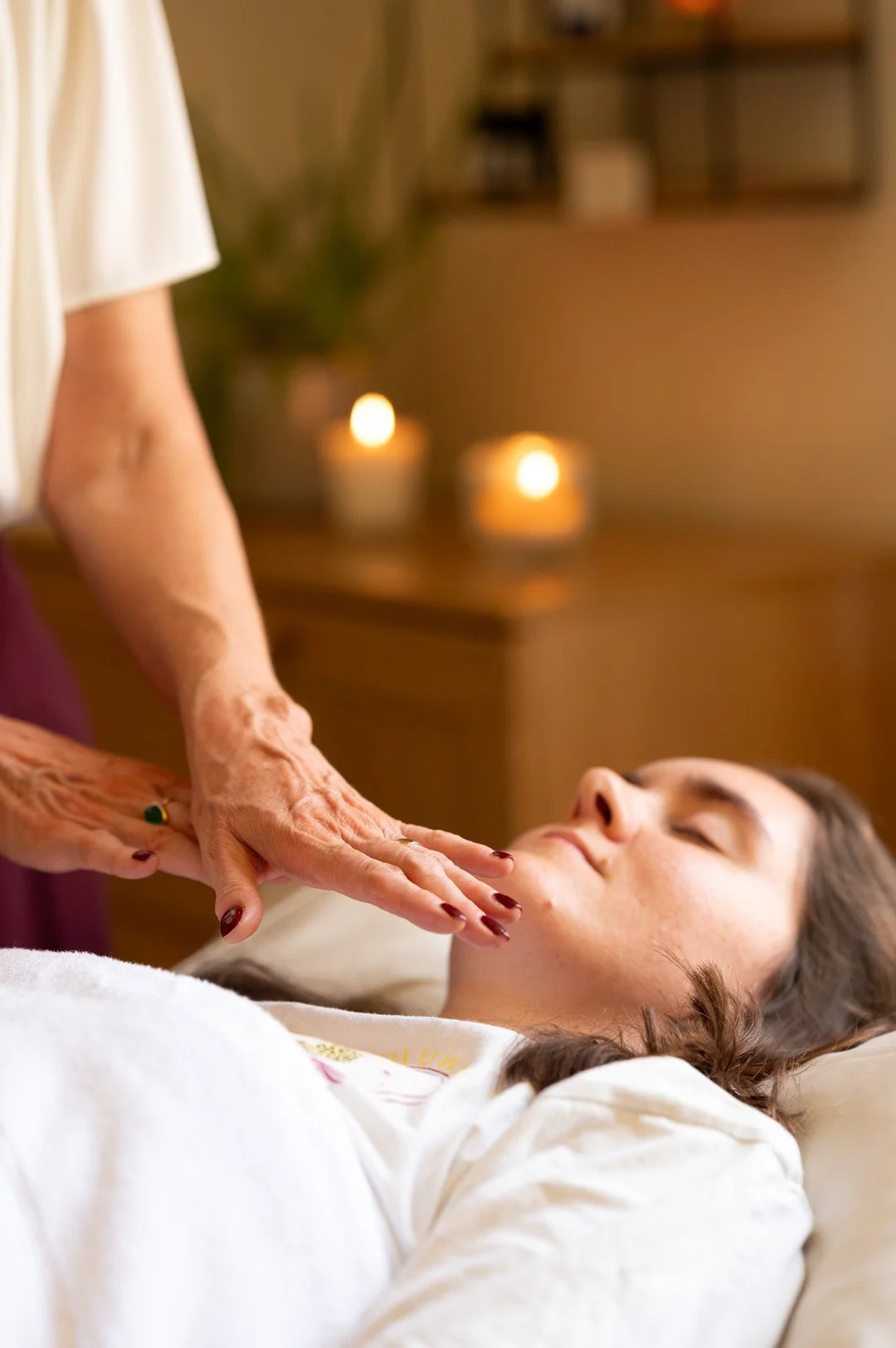 A woman receiving reiki from Julie in a relaxing spa setting with lit candles in the background.