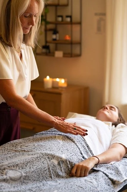 Julie is giving a healing Reiki treatment to a person lying on a bed in a cozy room with candles in the background.