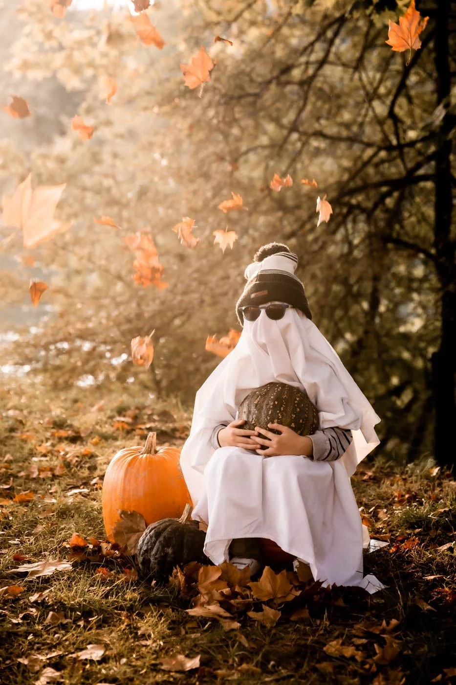 Enfant déguisé en fantome drap blanc avec lunettes de soleil tenant une courge dans une foret de feuilles rousses