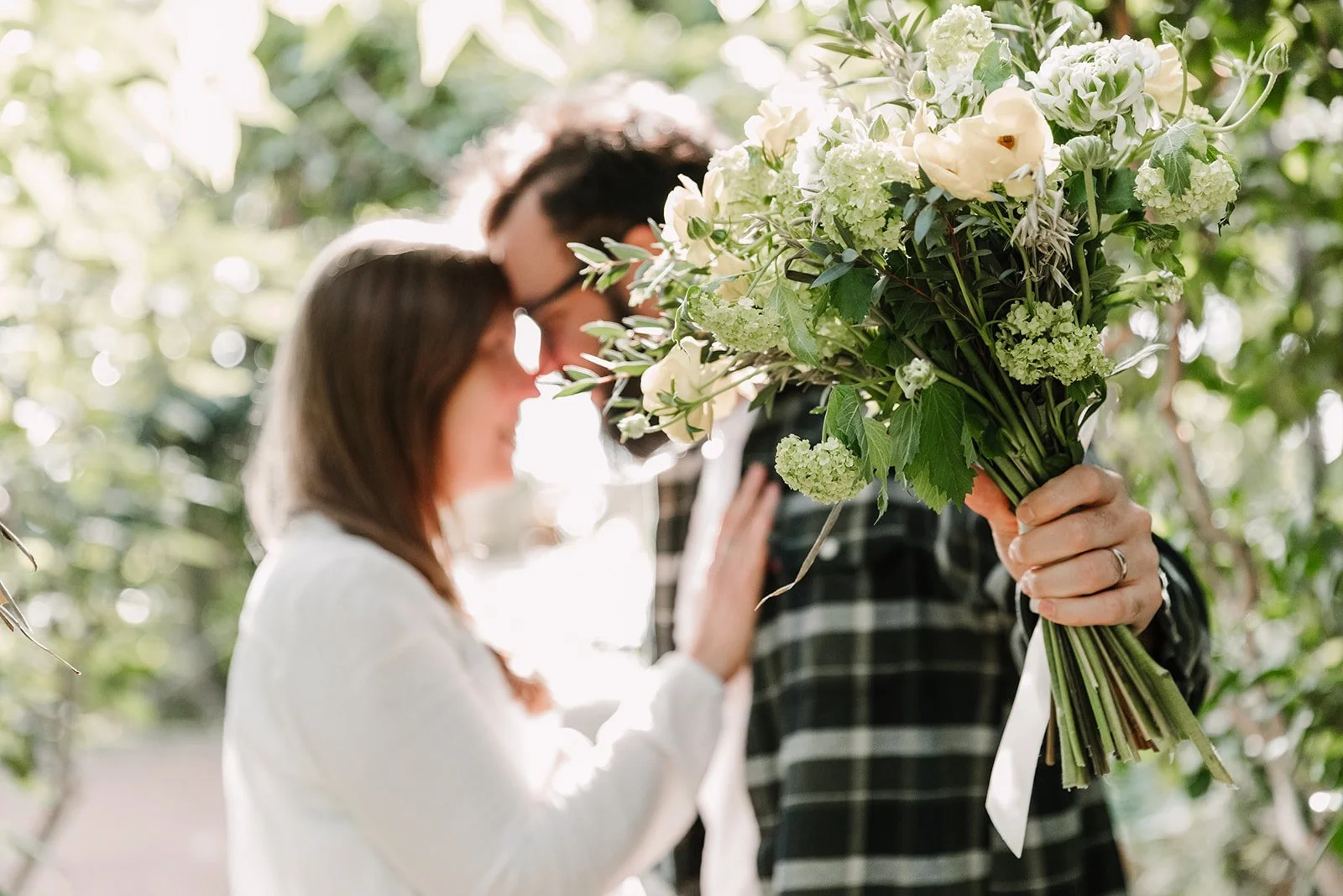 Couple front contre front en arriere plan flou tenant au premier plan un bouquet champetre de fleurs blanches