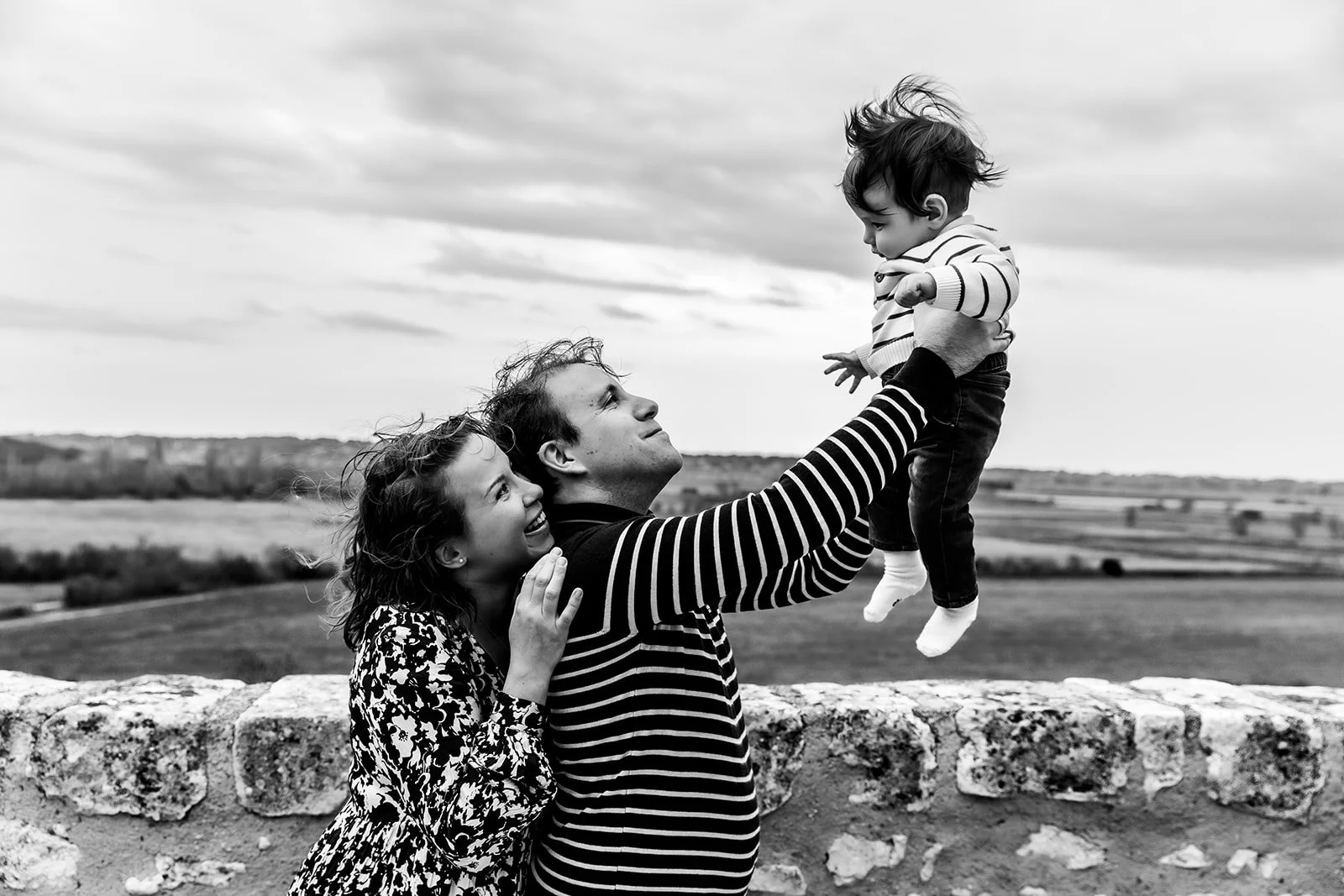 Maman appuyée sur papa soulevant bebe devant panorama nature photo noir blanc