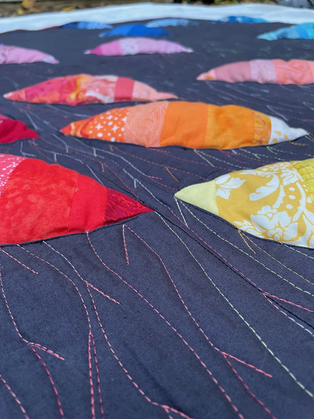  Image: detail of a quilt with a black background and 3-dimensional seed shapes in multiple colors. The stitching is done in wavy, forked lines, in thread that changes color. Click to read more about the quilt. 