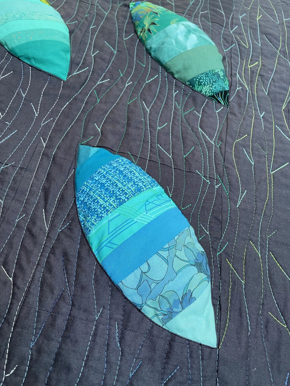  Image: detail of a quilt with a black background and 3-dimensional seed shapes in multiple colors. The stitching is done in wavy, forked lines, in thread that changes color. Click to read more about the quilt. 