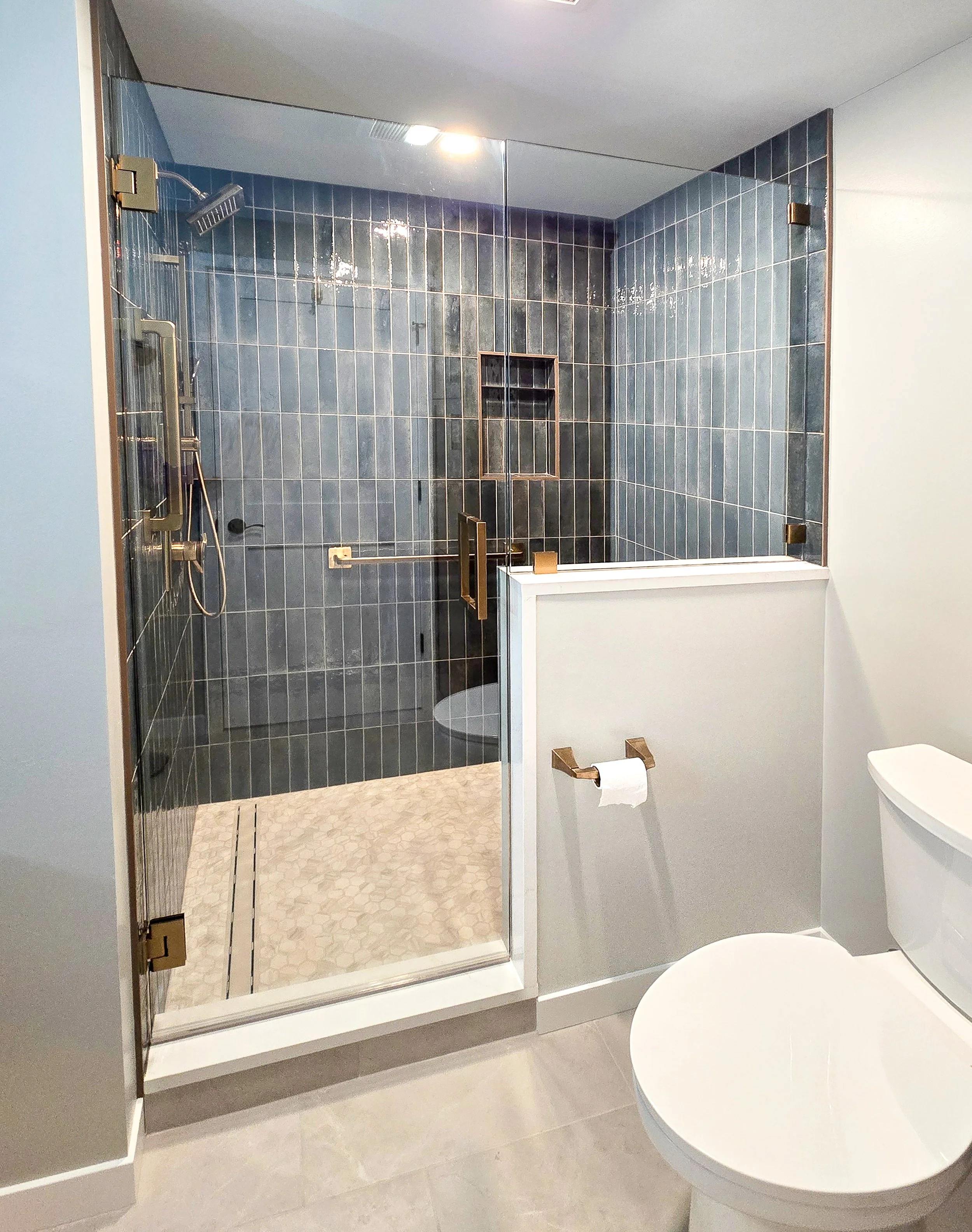 Modern hand-painted tile and glass-enclosed shower with gold fixtures.