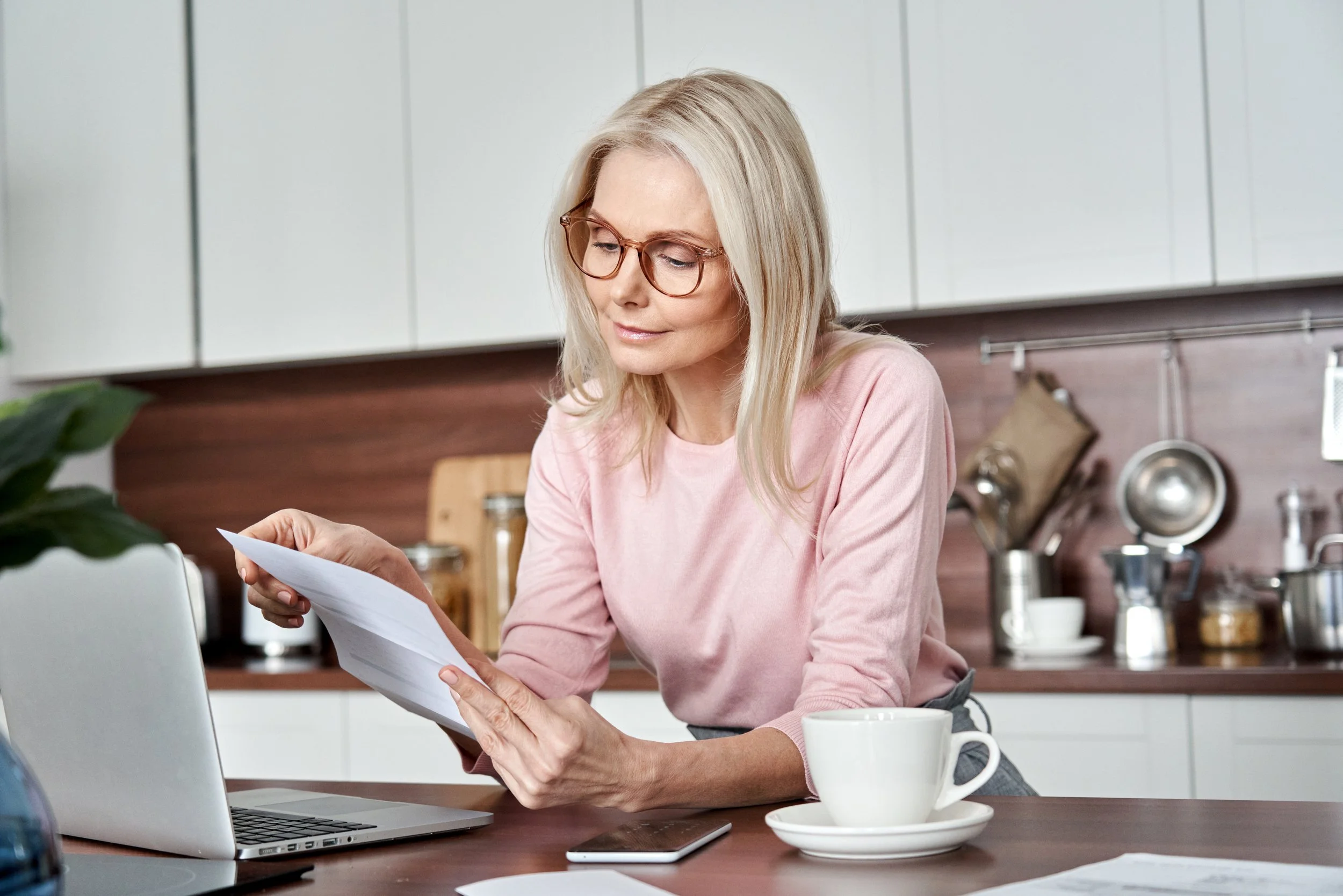 Print media can positively impact donations to nonprofit fundraising campaigns. This image depicts an older woman looking at a direct mail fundraising letter at her kitchen counter, smiling about the news from an organization she supports.