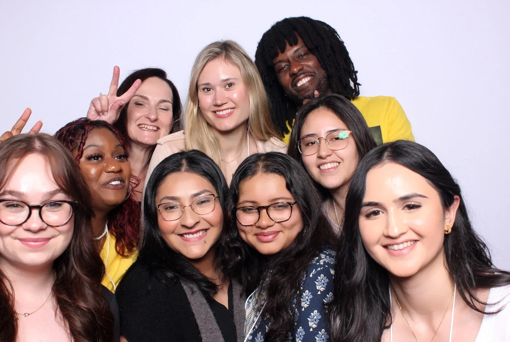 Group of diverse women and one man smiling, posing for a photo against a plain white background.