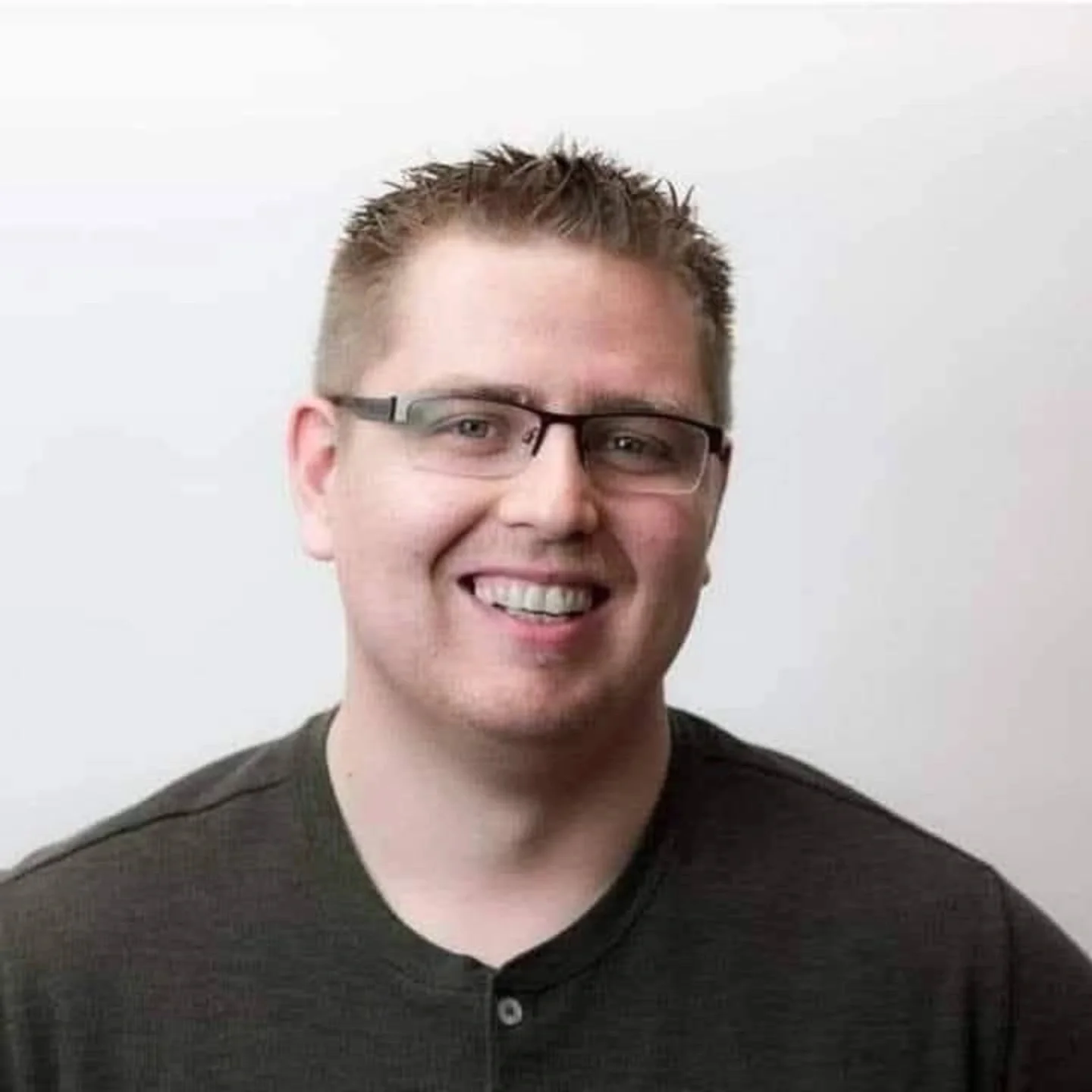 A man with short hair, glasses, and black tee shirt smiles at the camera