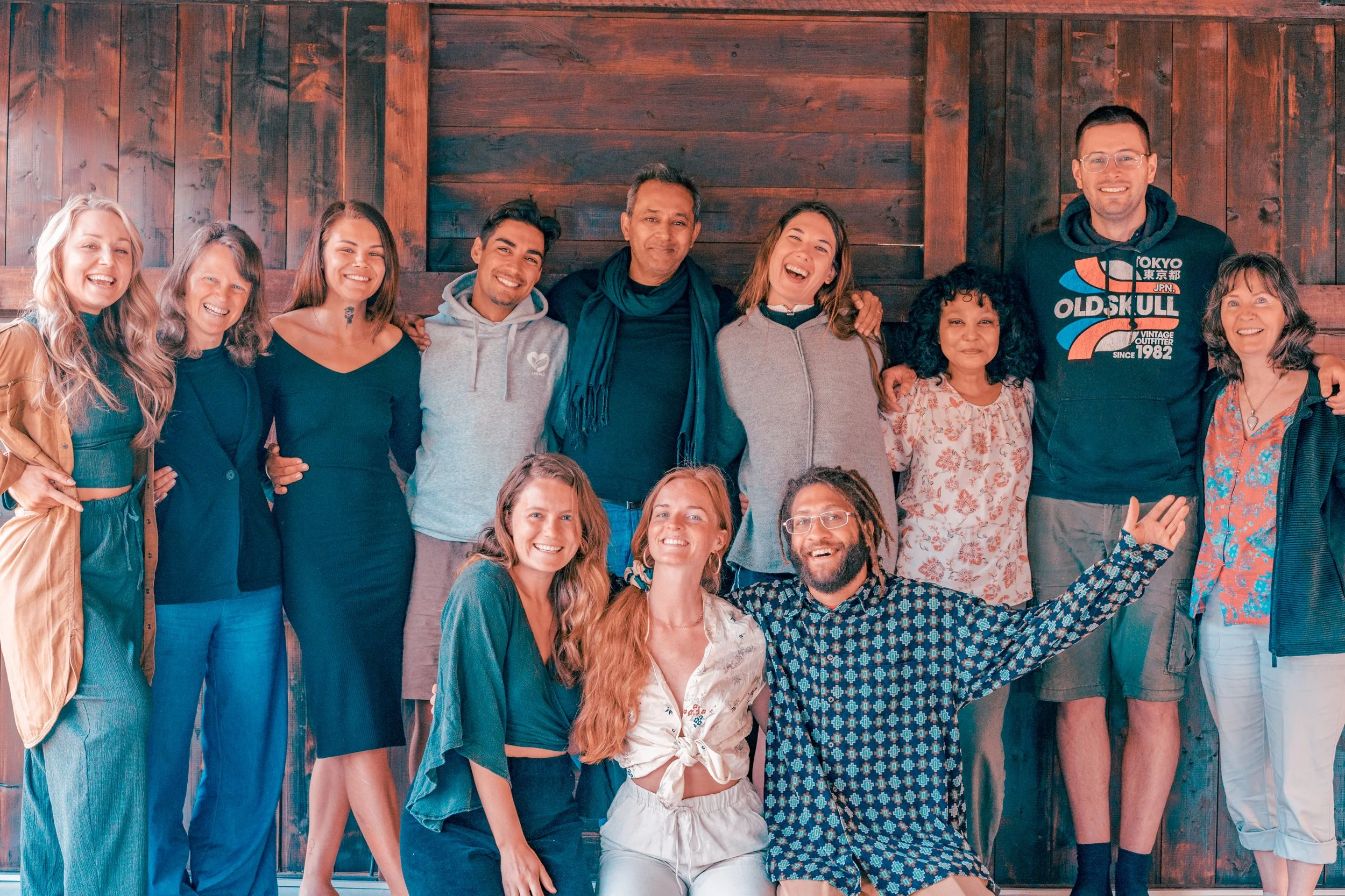 A diverse group of smiling people posing together in front of a wooden wall.