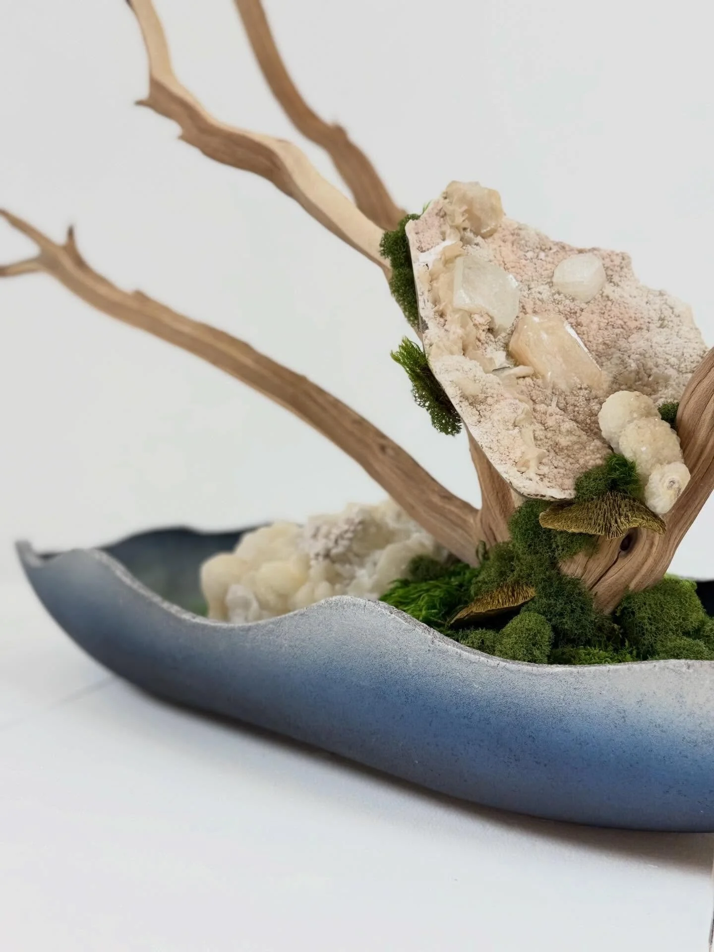 The soft blue vessel grounds the piece with a calm, coastal tone creating contrast against the raw wood, crystal textures, and organic movement. It&rsquo;s a balance of serenity and structure, where every element feels both elevated and effortless.

