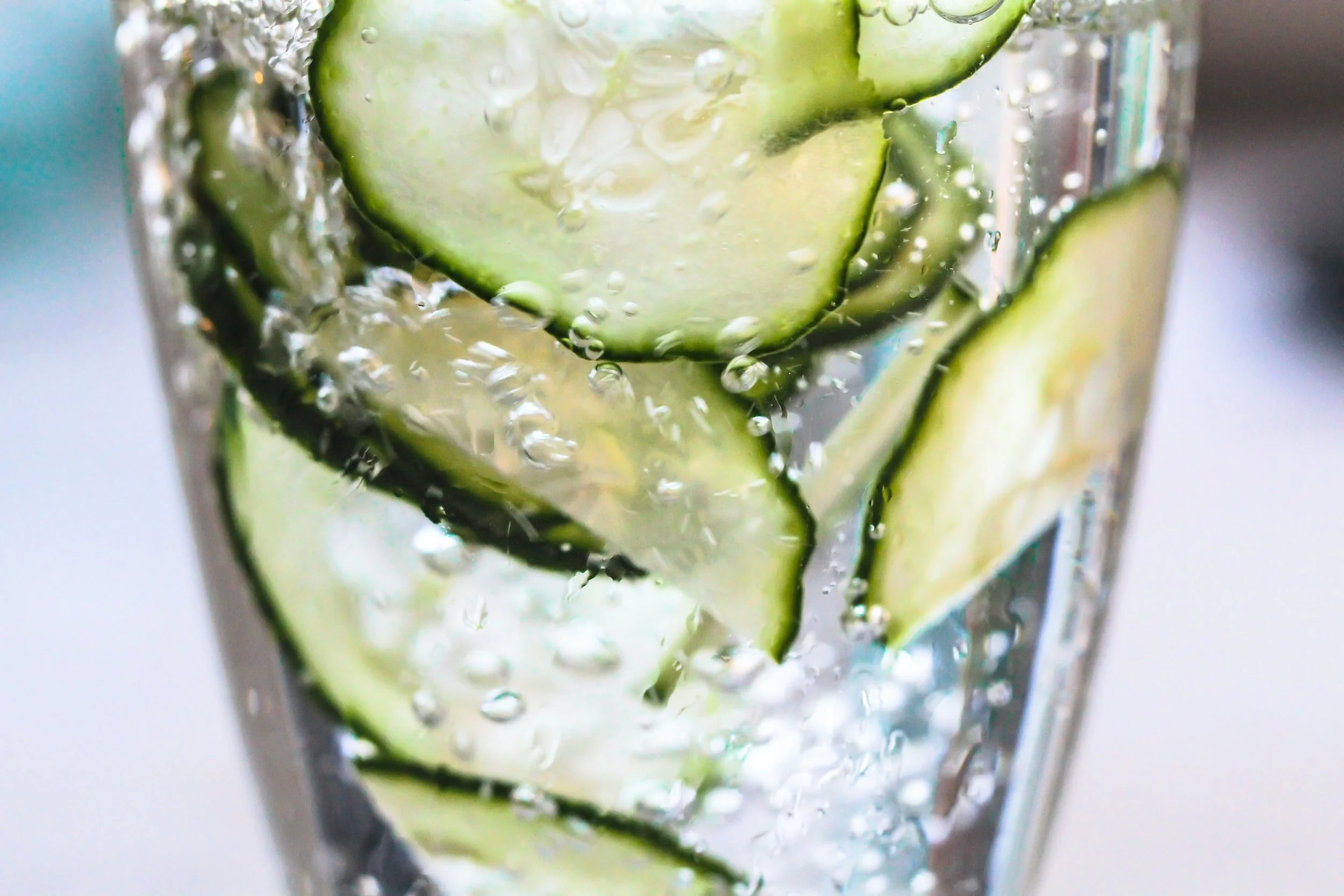 Close-up of a glass of sparkling water with cucumber slices inside.