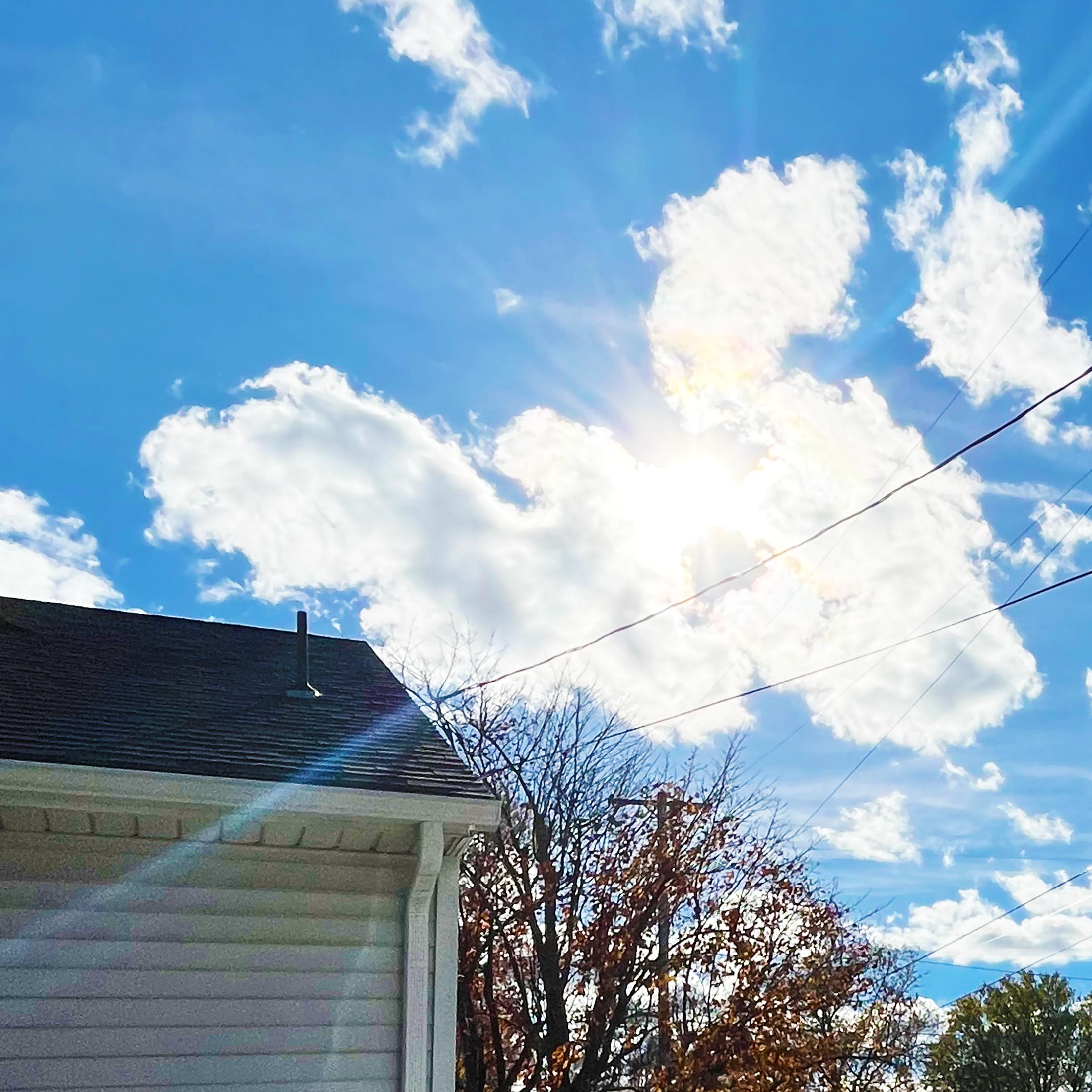 sun shining through angel-shaped cloud in blue winter sky above trees and roof of a home