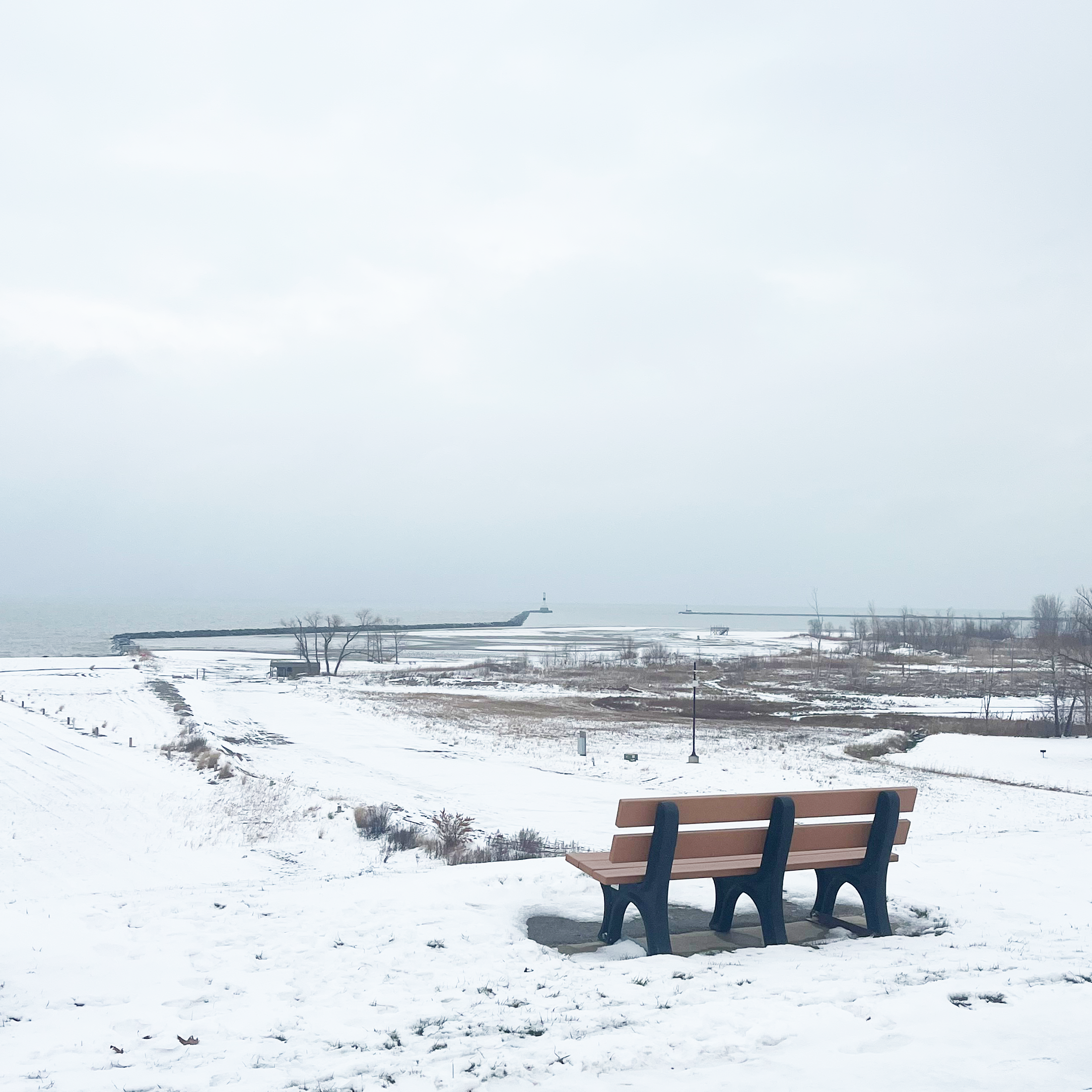bench on a snowy bluff overlooking Lake Erie and lighthouse
