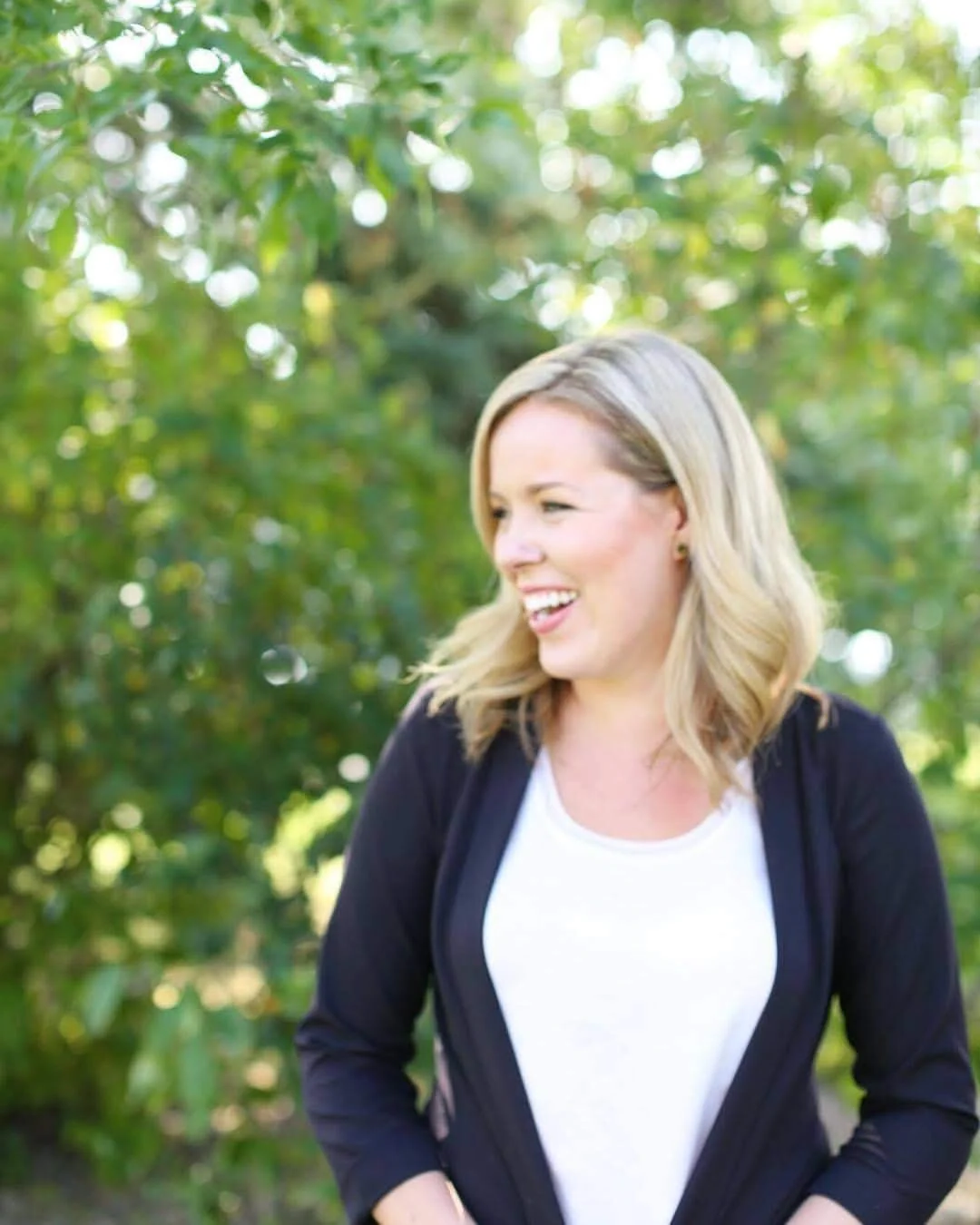 A blonde woman laughing with a background of trees