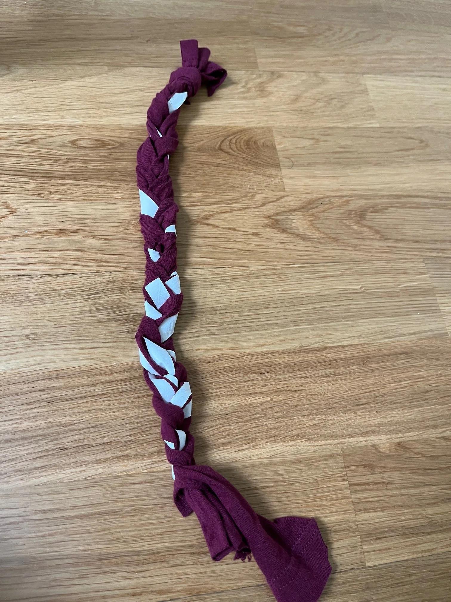 A grief braid made of maroon and white fabric strips laid on a wooden surface.