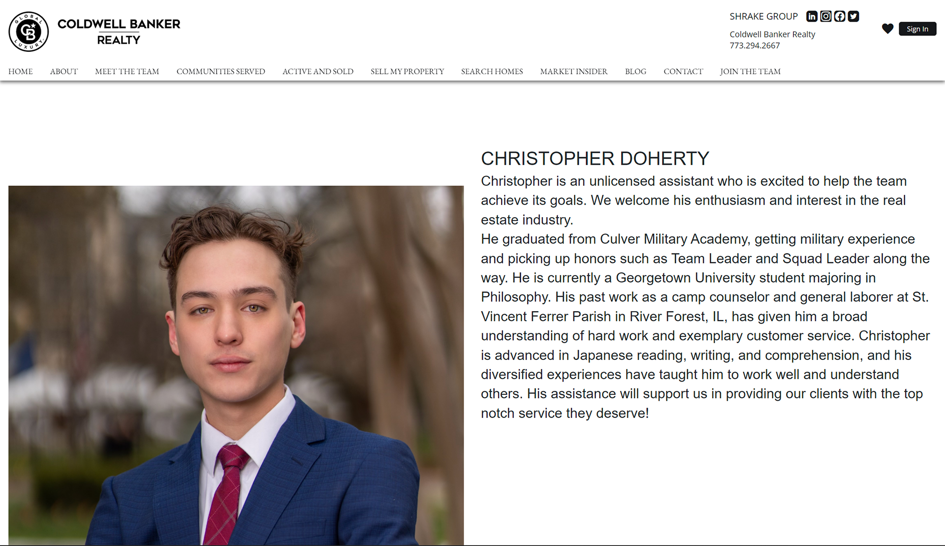 Portrait of Christopher Doherty wearing a blue suit with a red tie, standing outdoors with blurred trees in the background.