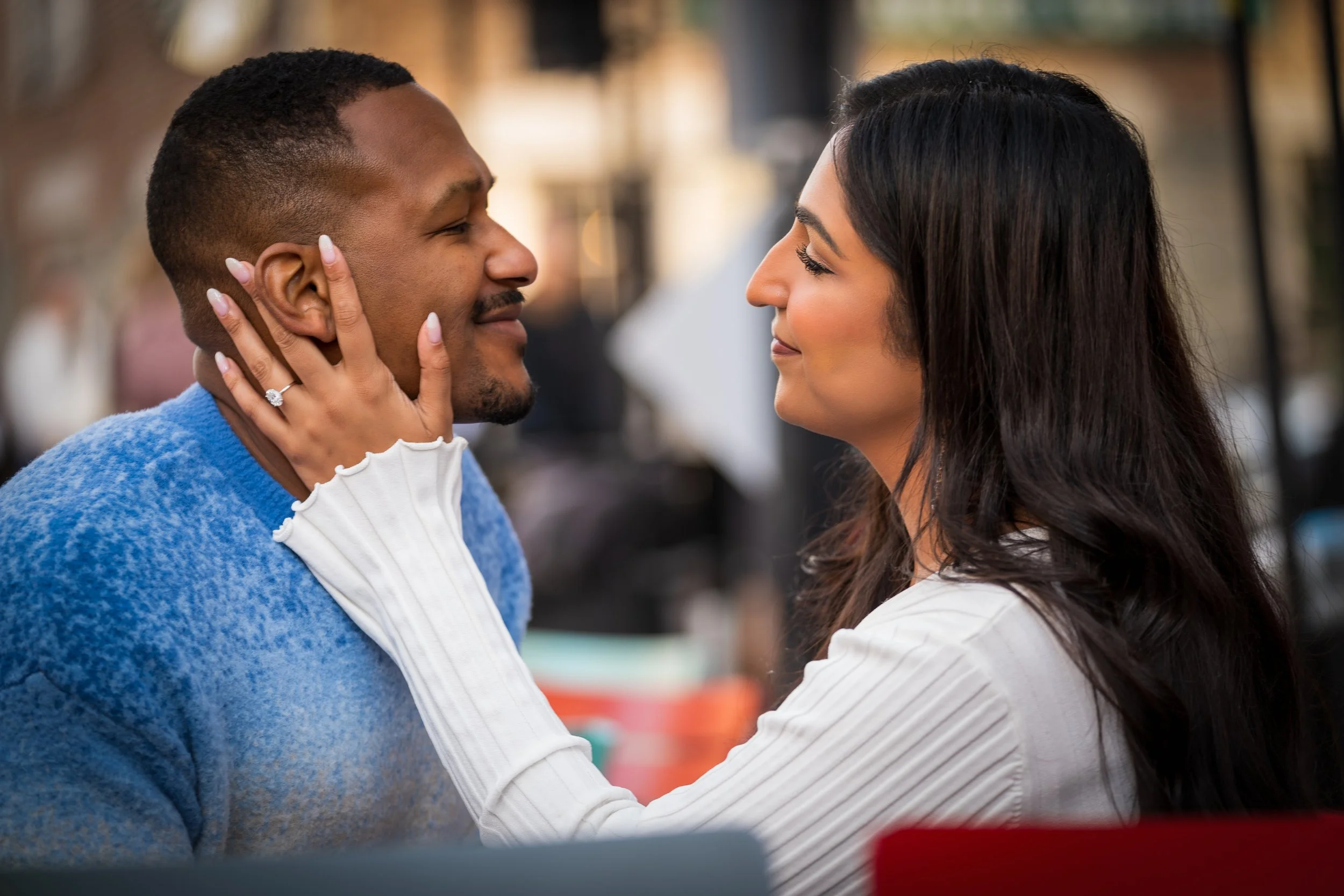 A man and woman looking at each other with smiles, the woman's hand with a wedding ring on her finger gently touching the man's face.