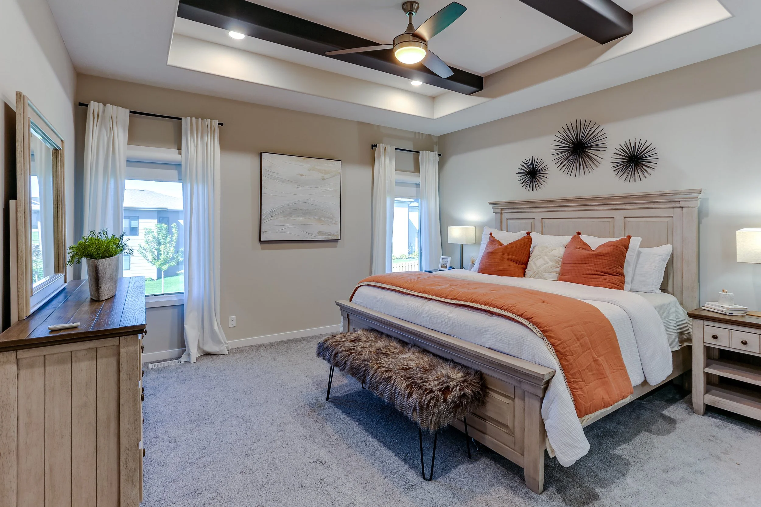 A bedroom with a large bed featuring orange and white bedding, a fur-covered bench at the foot, wooden furniture, and wall decorations.