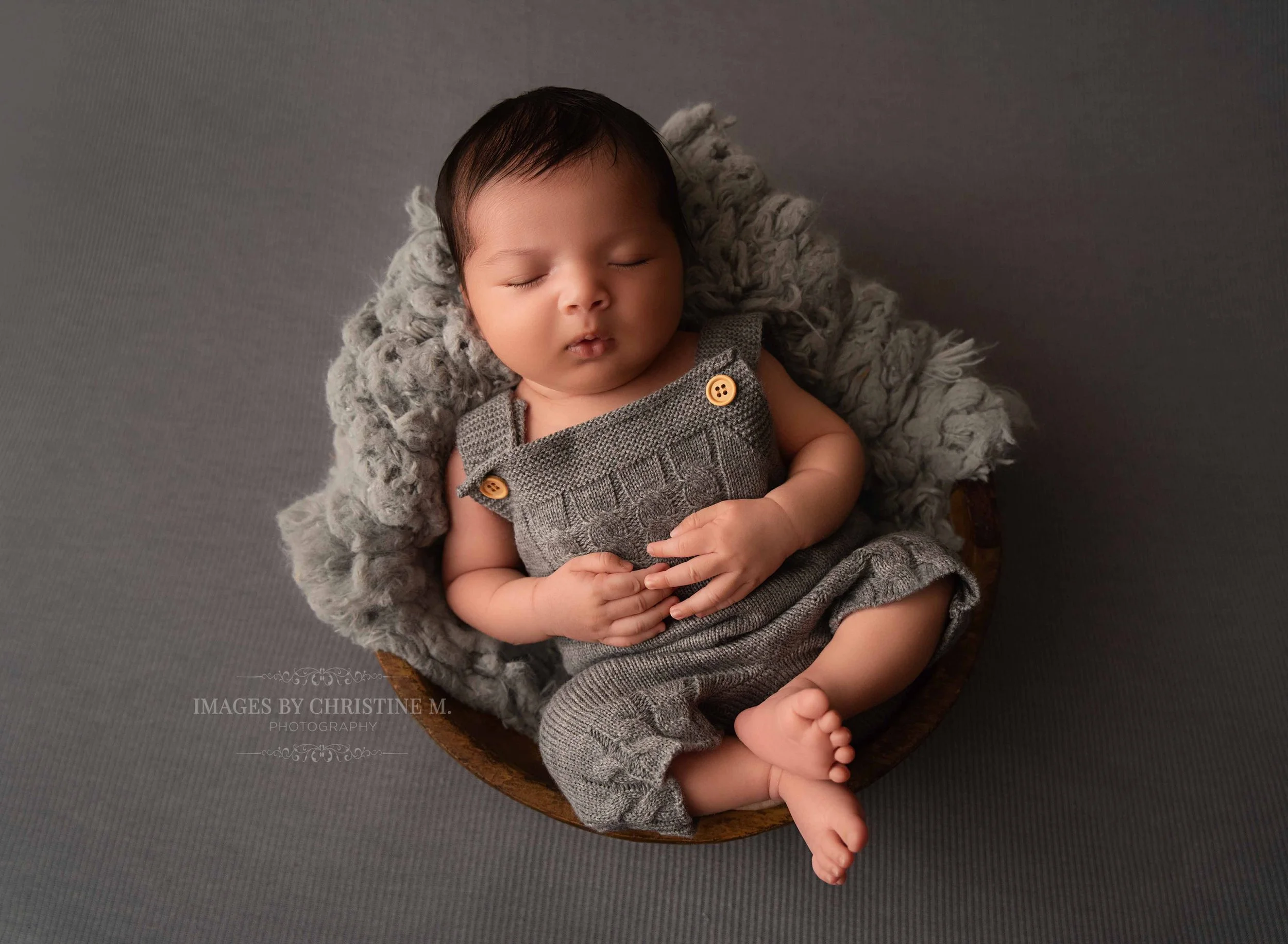 Newborn baby boy on his back in a bowl wearing a grey romper