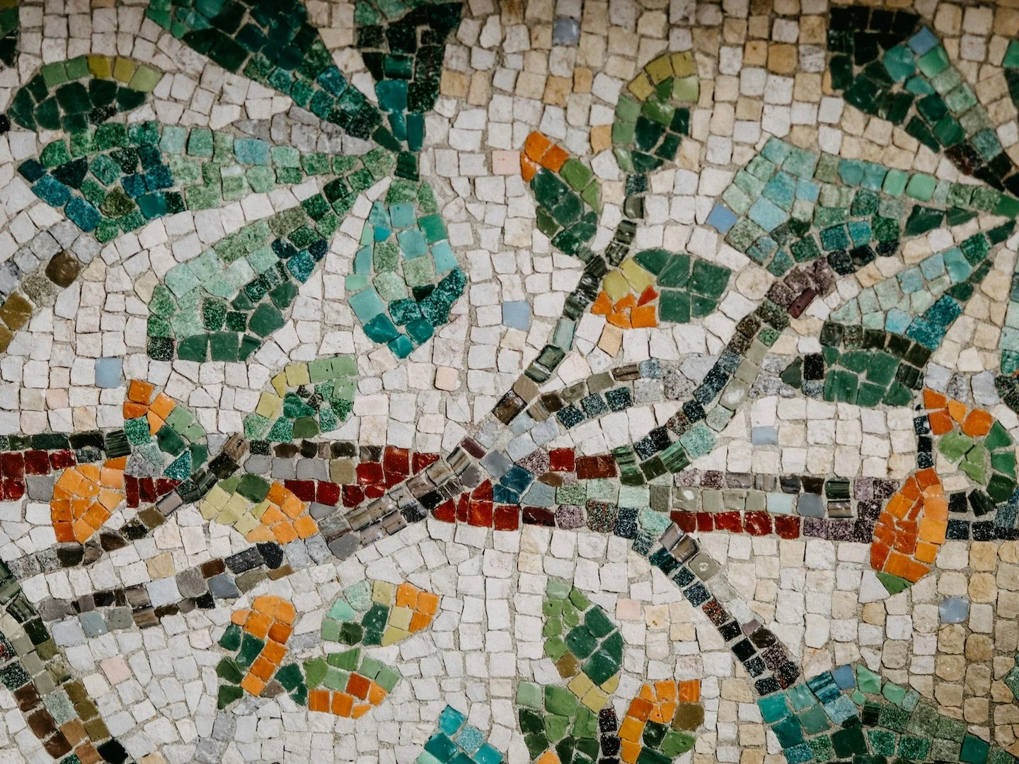 Close-up of a mosaic with a butterfly and floral design made of small colored tiles, featuring green, orange, red, black, and white tiles.