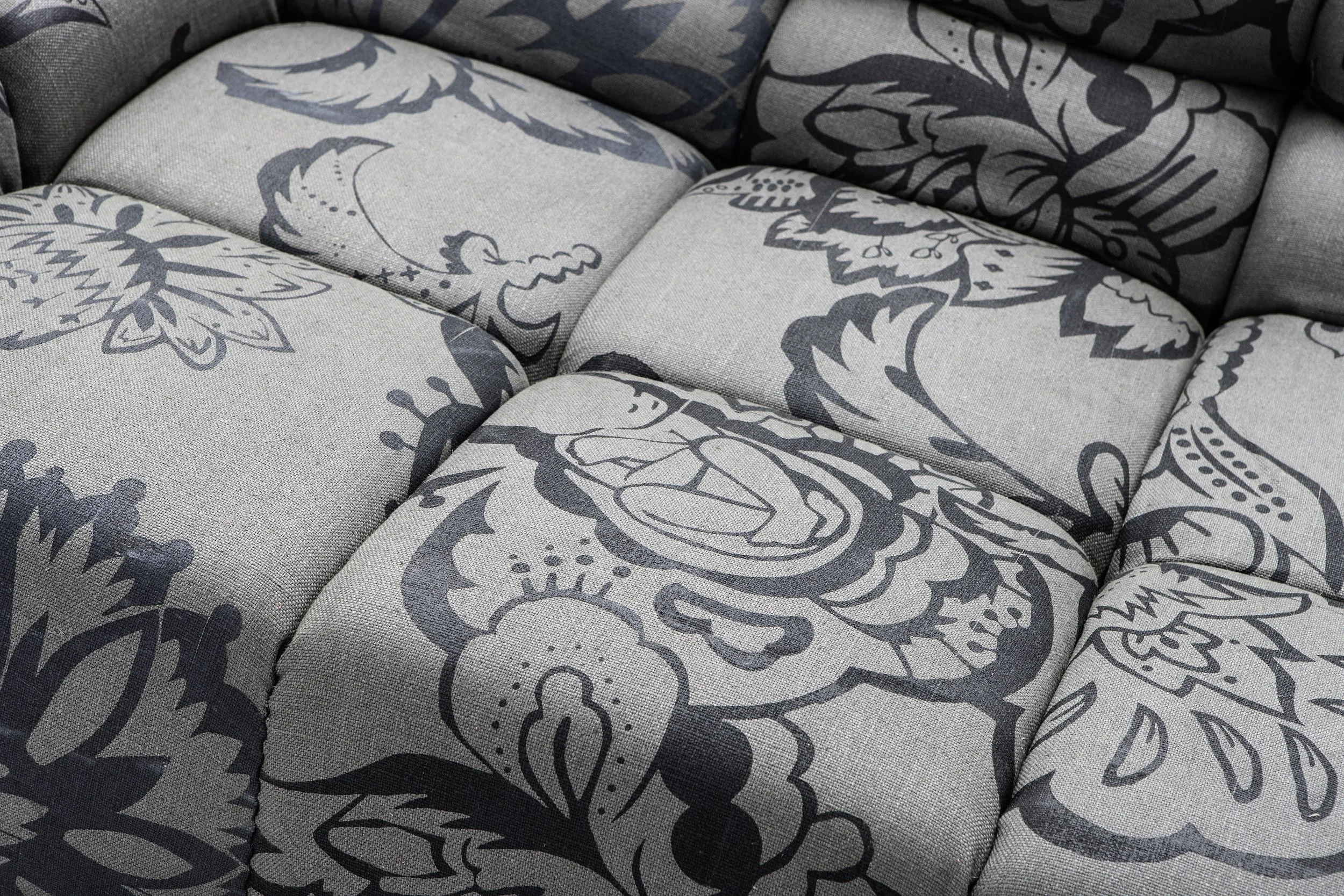 Close-up of a tufted sofa upholstered in a grey fabric with a repeating ornamental floral pattern.