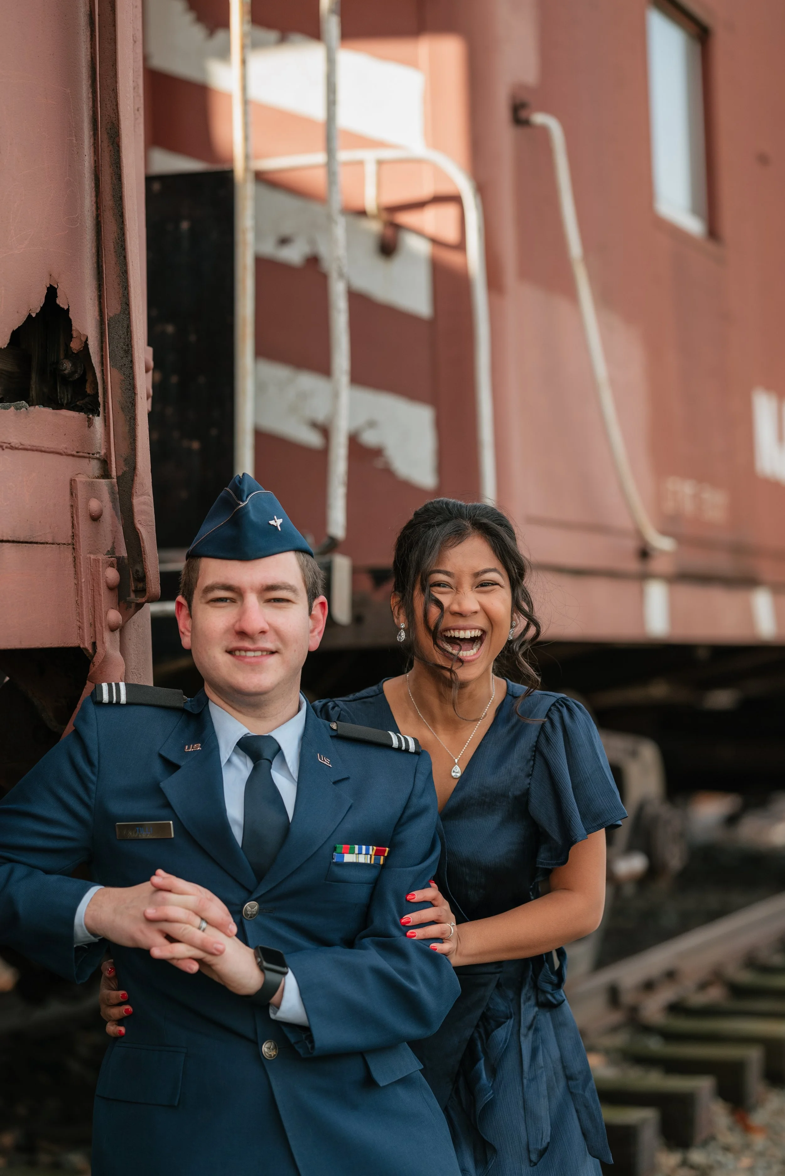 A woman and a man in military uniform smiling and posing in front of a train car.