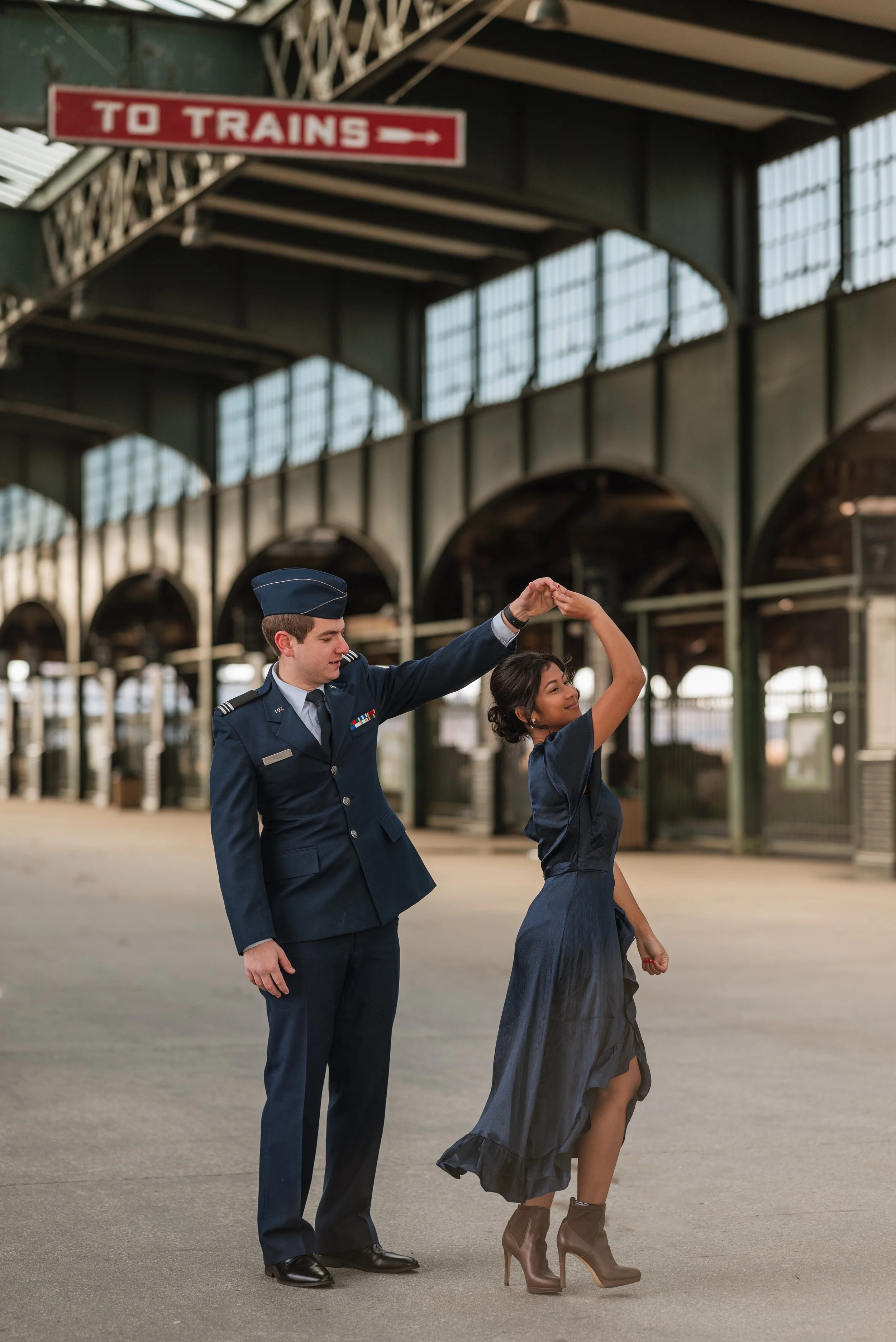 A military officer in uniform dancing with a woman at a train station.
