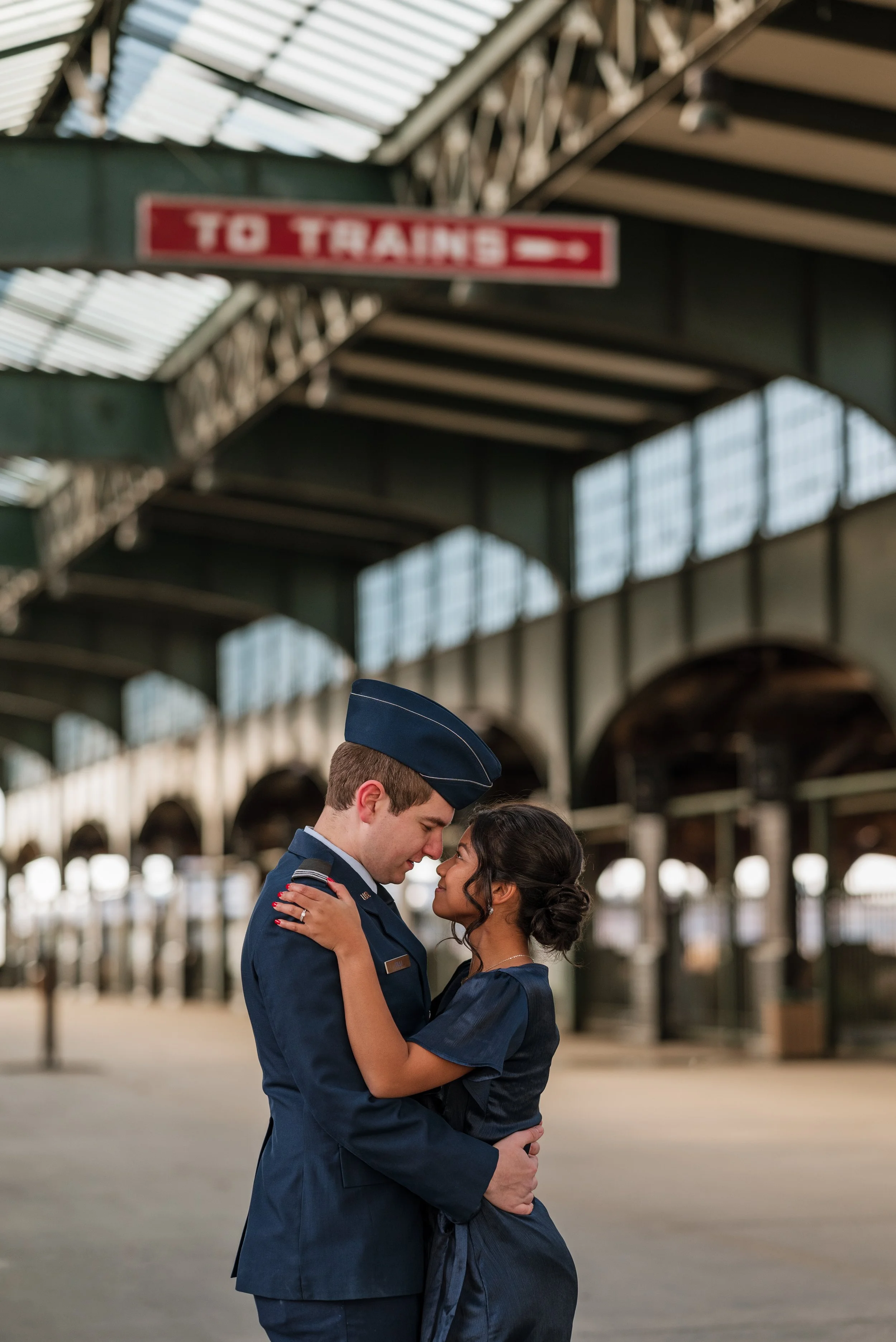 A couple in military uniform embracing on a train platform.
